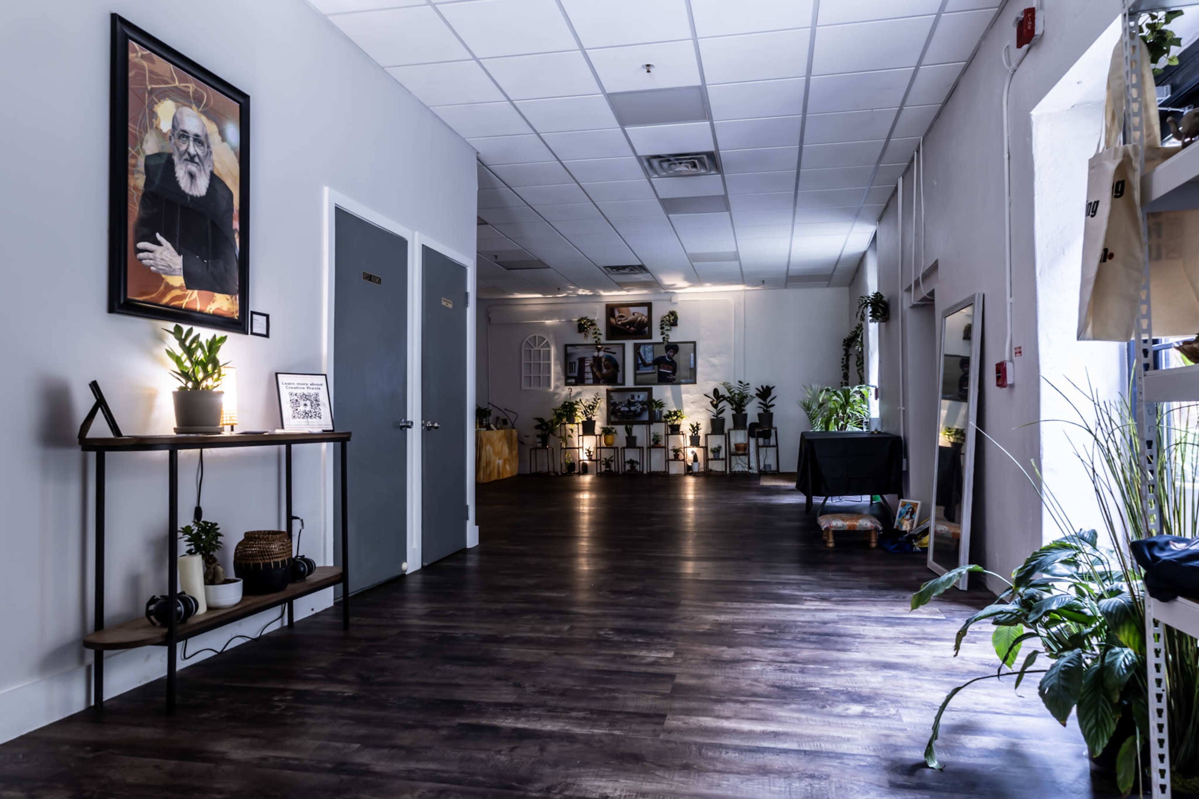 The image depicts a spacious, well-lit hallway adorned with plants and artwork, leading to an area with various decorative displays.