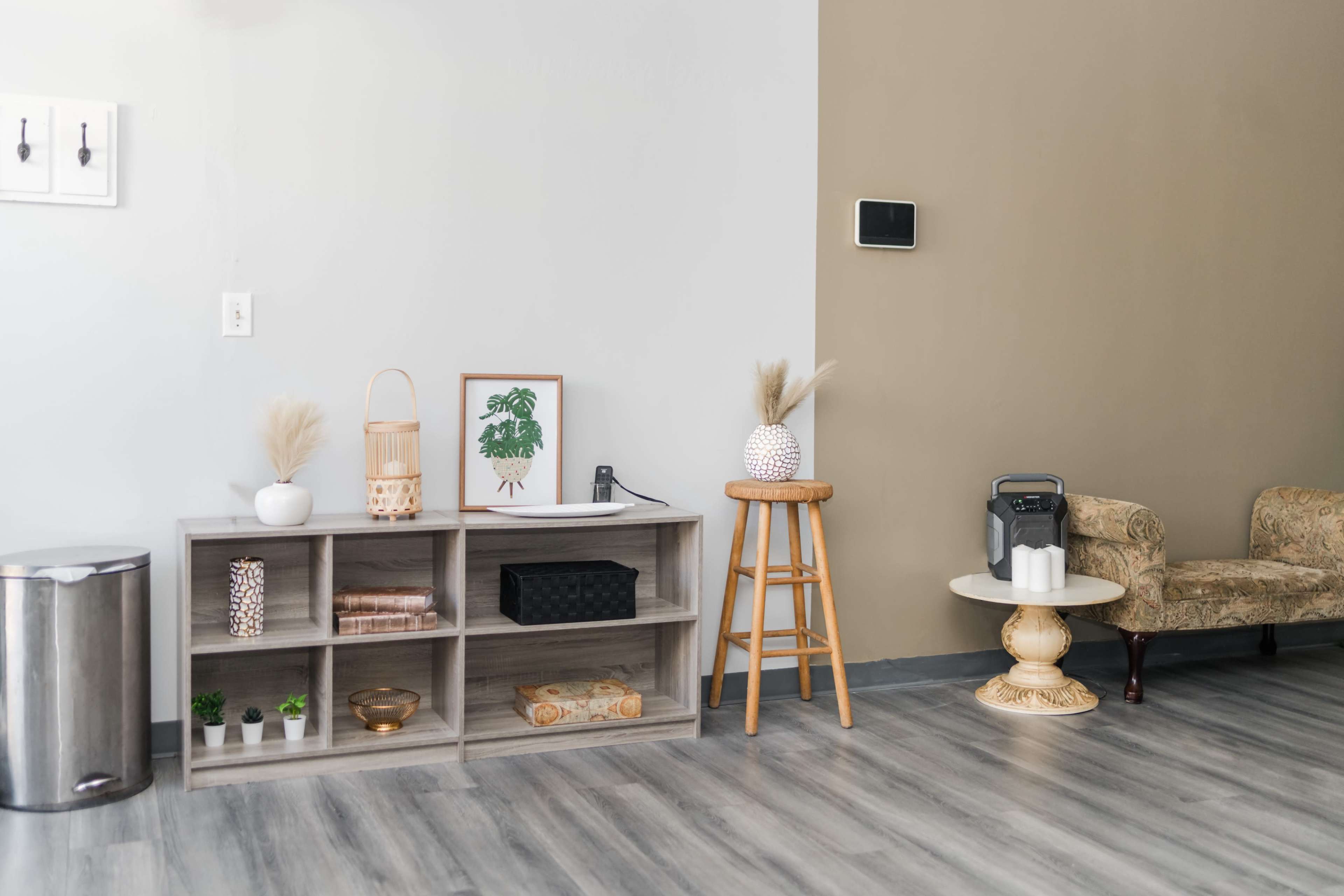 A modern living space with a shelving unit, decorative plants, a small table, and a patterned chair against a two-tone wall.