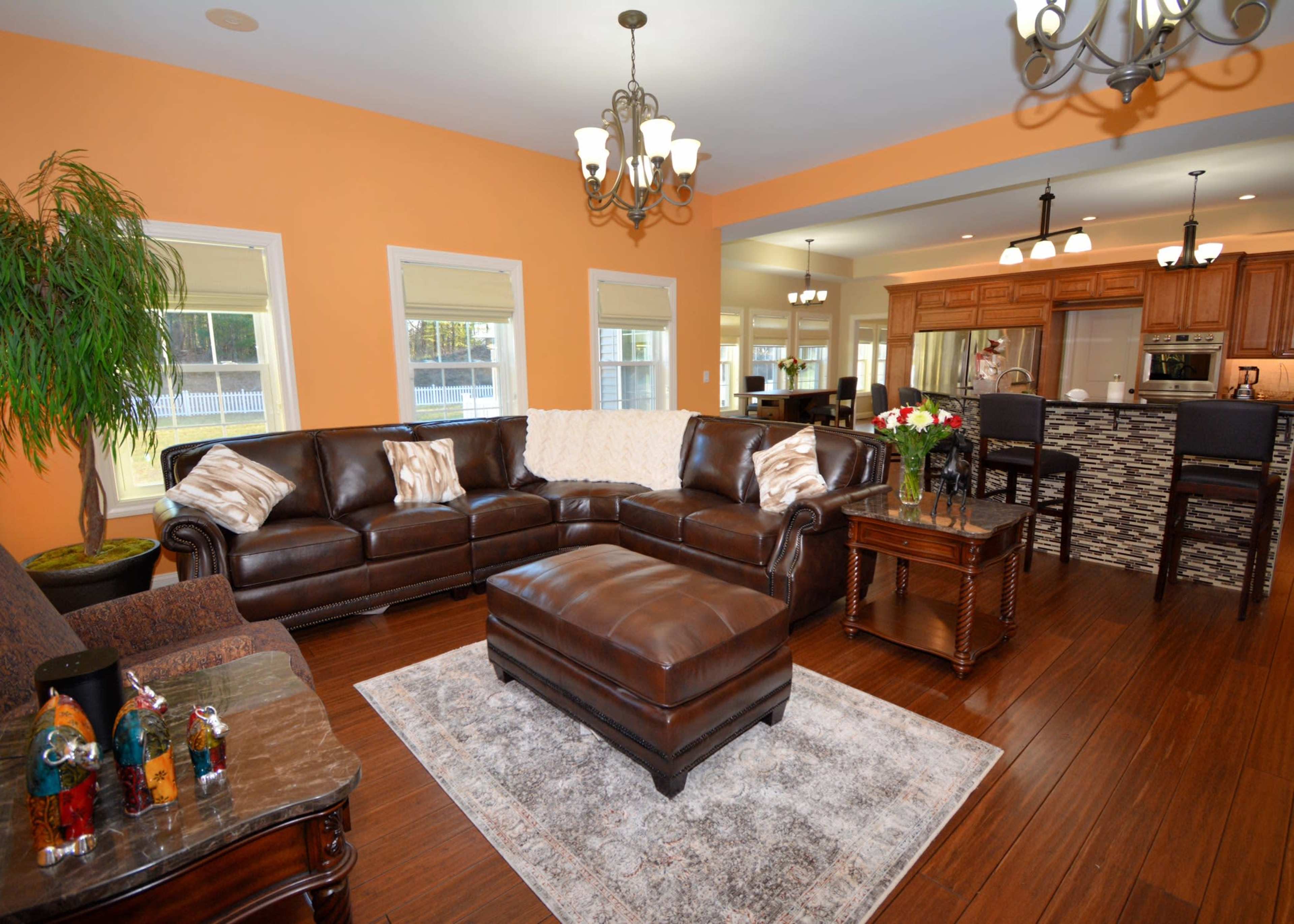 A modern living room features a brown leather sectional sofa, a coffee table, and a decorative rug, with an open kitchen visible in the background.