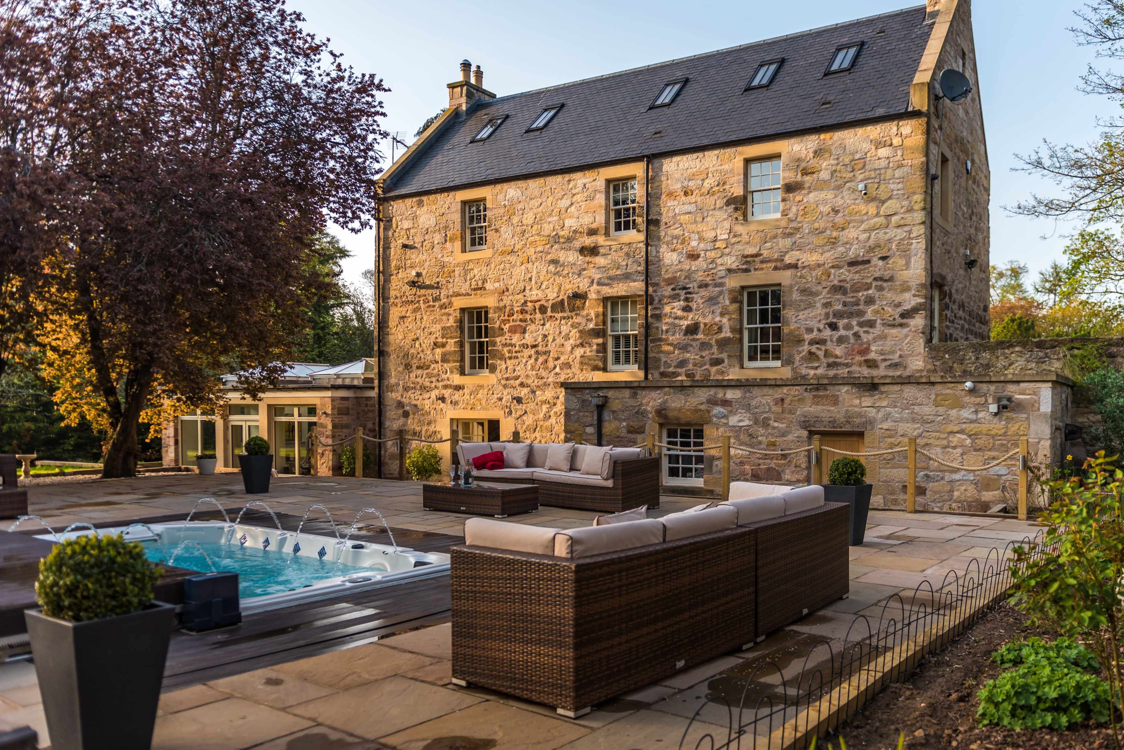 A stone house with a landscaped patio featuring outdoor seating and a hot tub.
