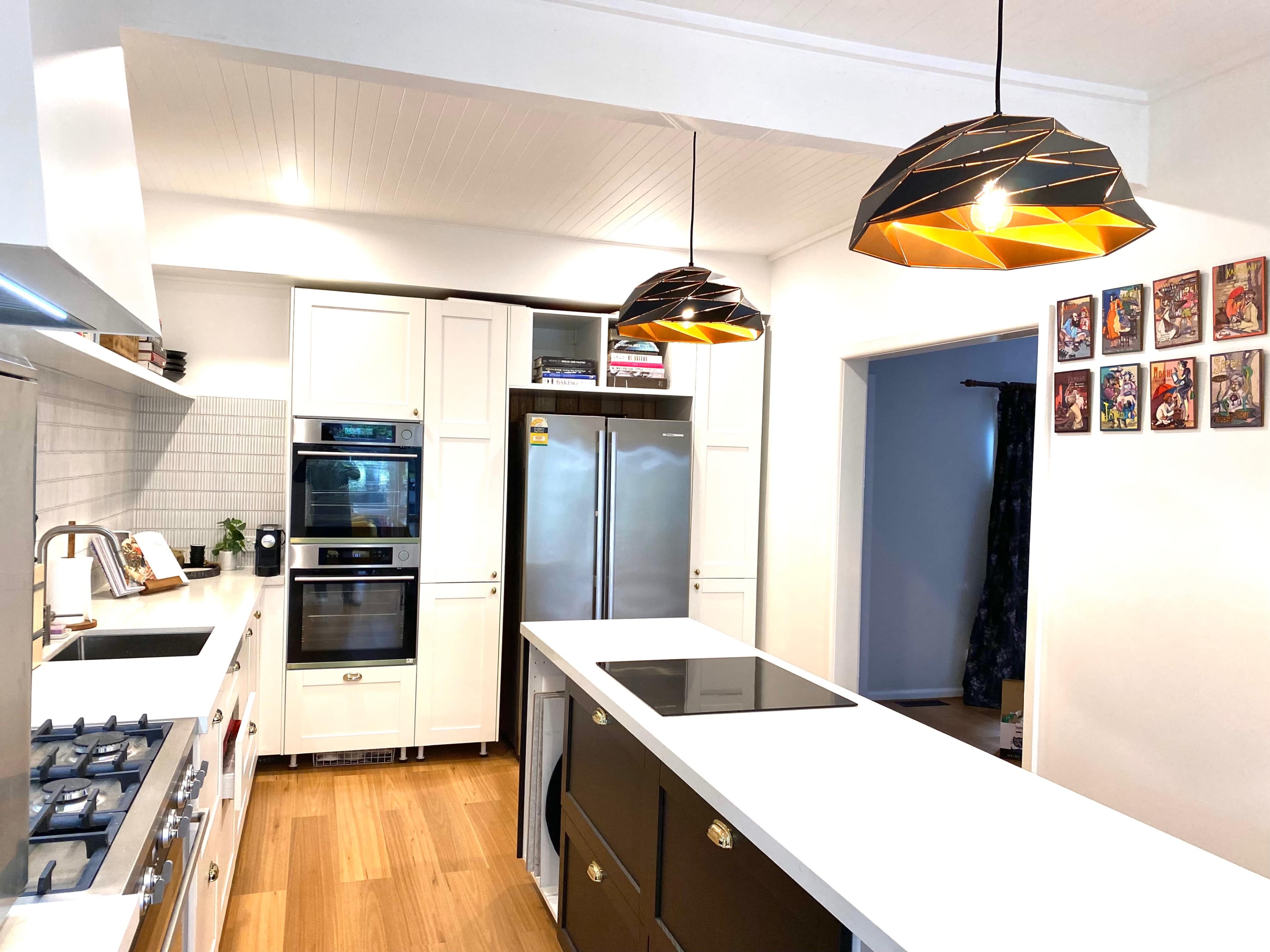 A modern kitchen featuring white cabinetry, stainless steel appliances, a central island with a cooktop, and two unique pendant lights above the island.