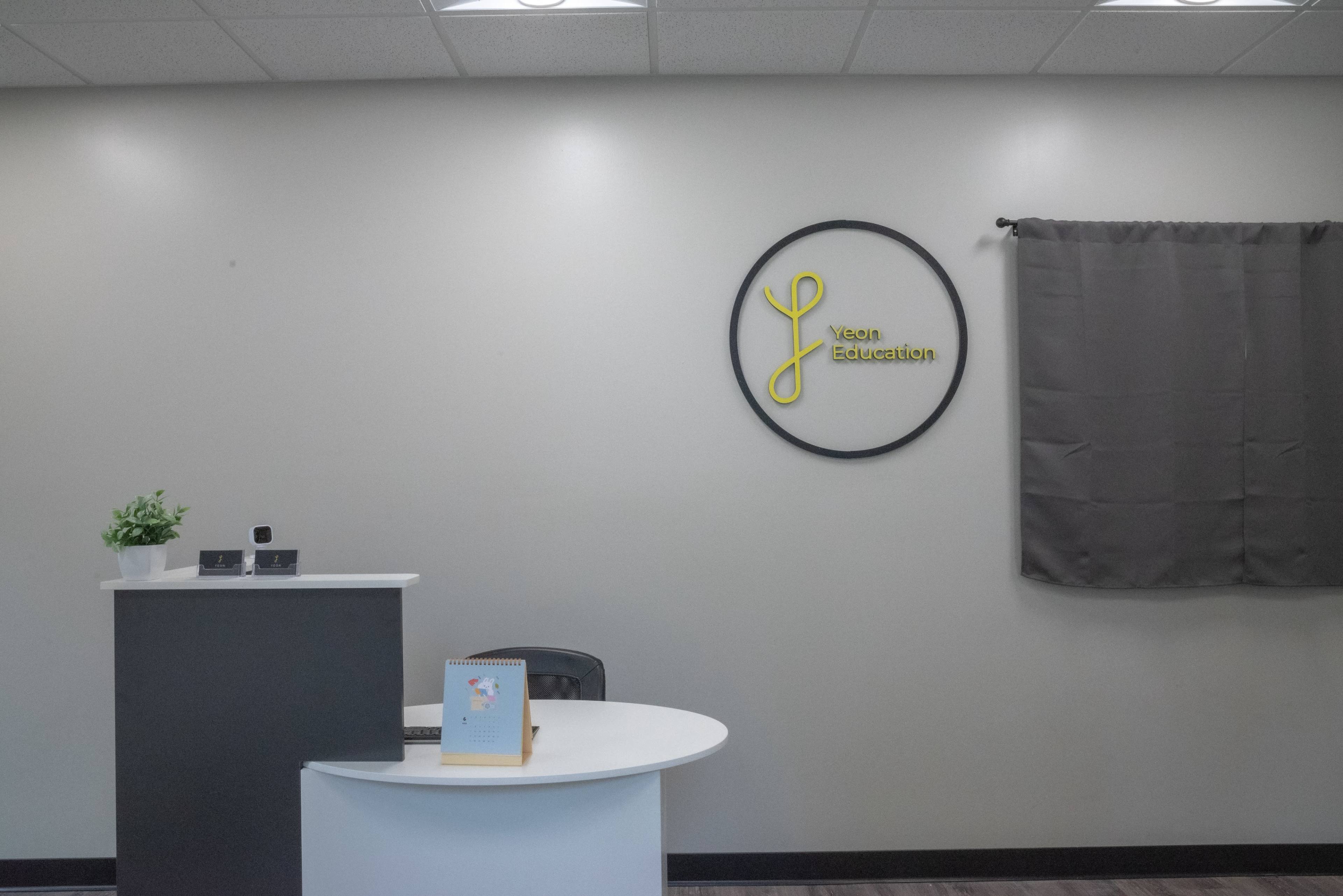 A reception area for a business called "Yean Education," featuring a circular wall sign, a counter, and a chair next to a window covered by a curtain.