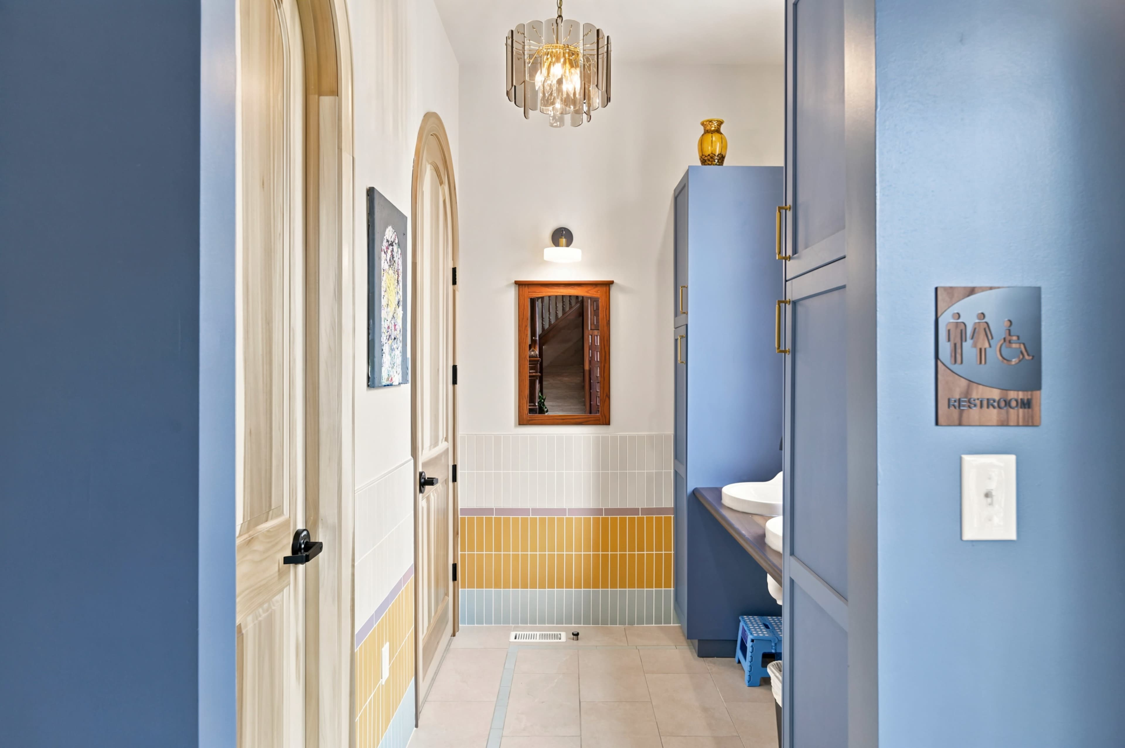 A brightly lit restroom area features a combination of blue and yellow wall colors, a decorative mirror, and modern fixtures.