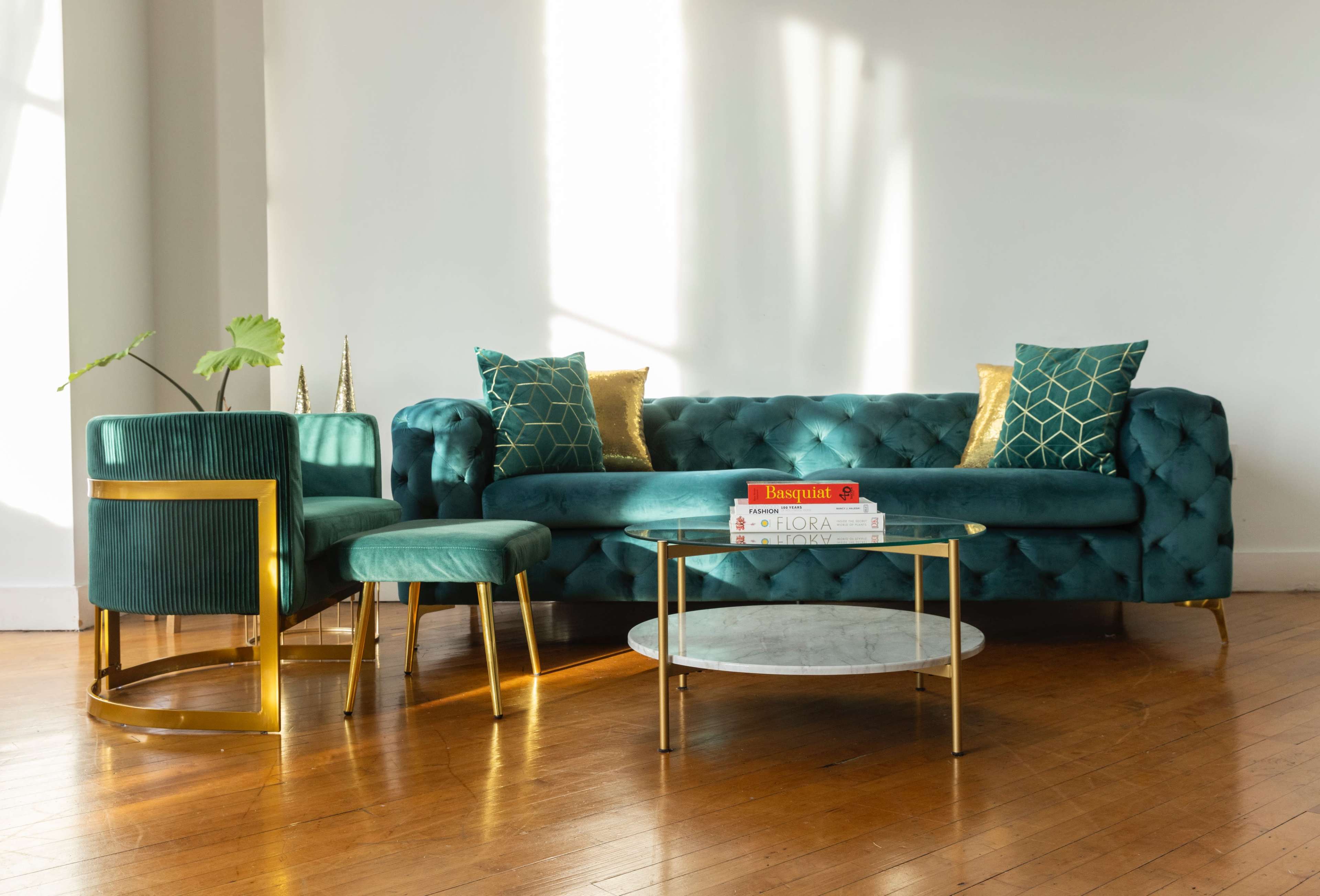 The image features a teal velvet sofa and armchair set with gold accents, accompanied by a round coffee table and decorative books on top.