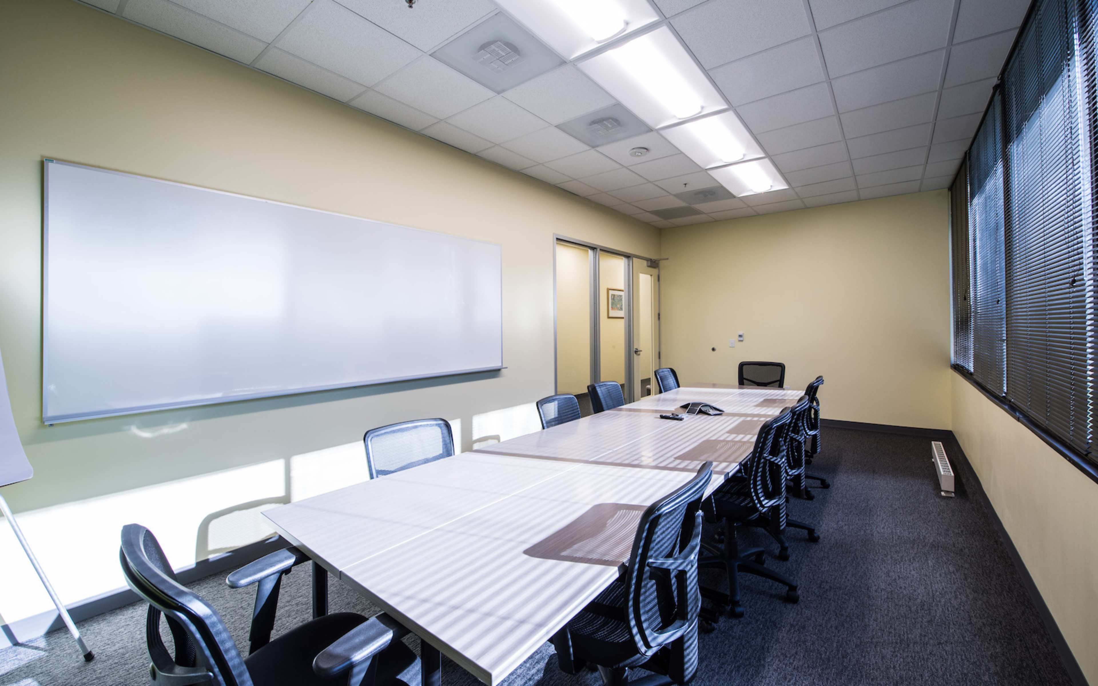 The image shows a conference room with a long table, several chairs, and a large whiteboard on one wall.