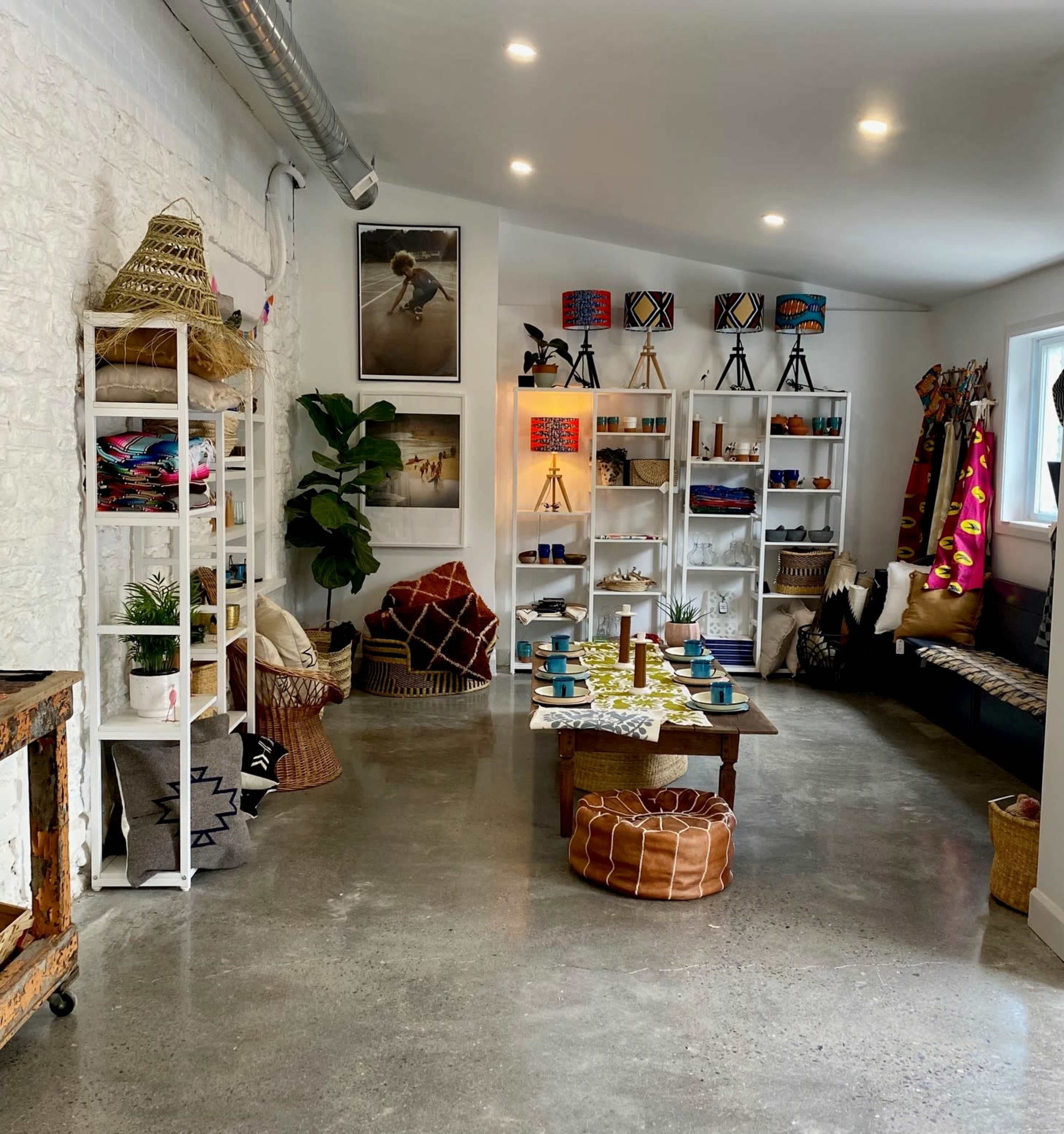 A modern interior space featuring shelves filled with decorative items, a wooden table set for dining, and various seating options including floor cushions and a bench.