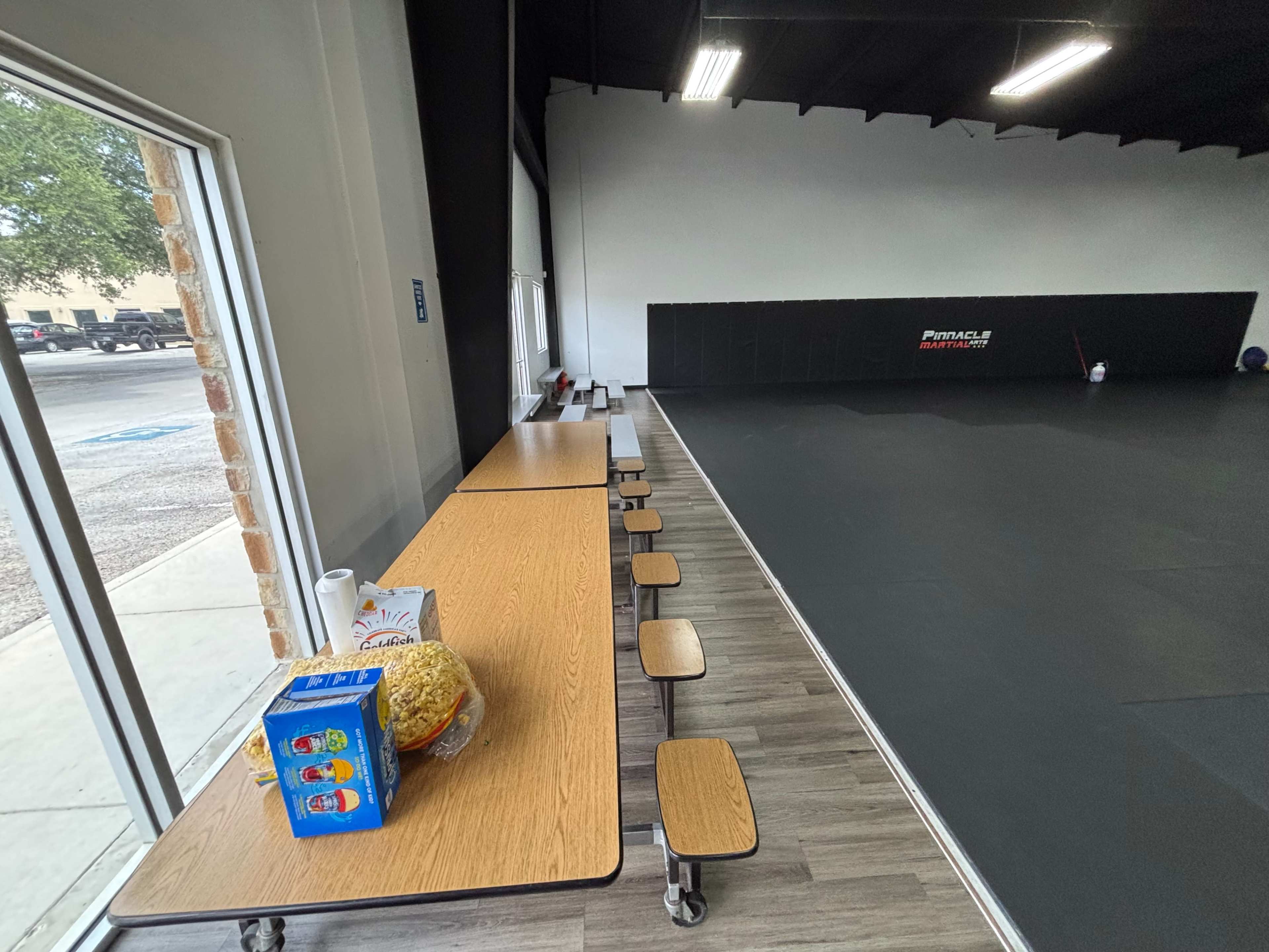A long table with several benches is positioned next to a large, open training space with a dark floor and mirrors.