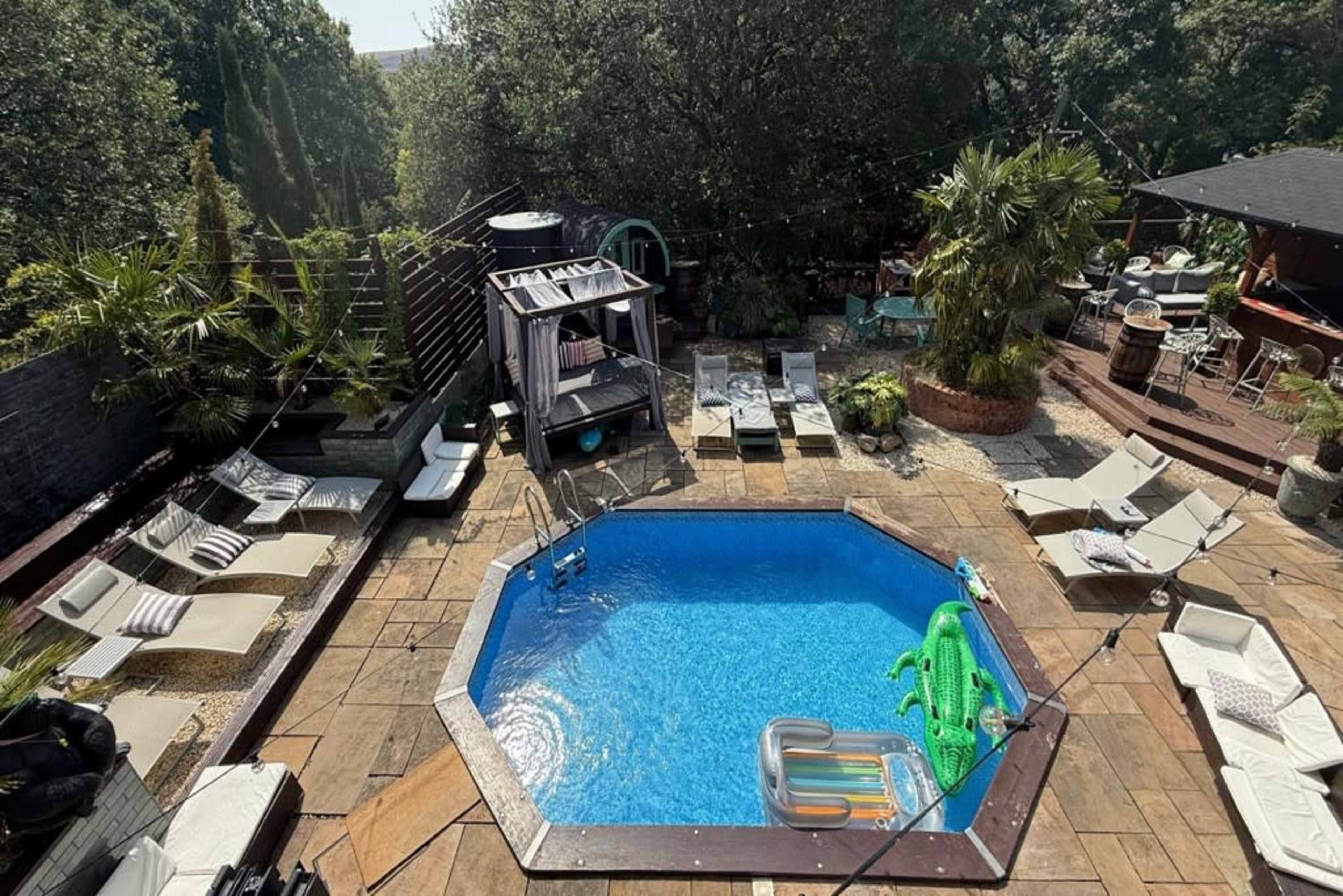 The image shows a landscaped backyard featuring an octagonal swimming pool surrounded by lounge chairs and tropical plants.