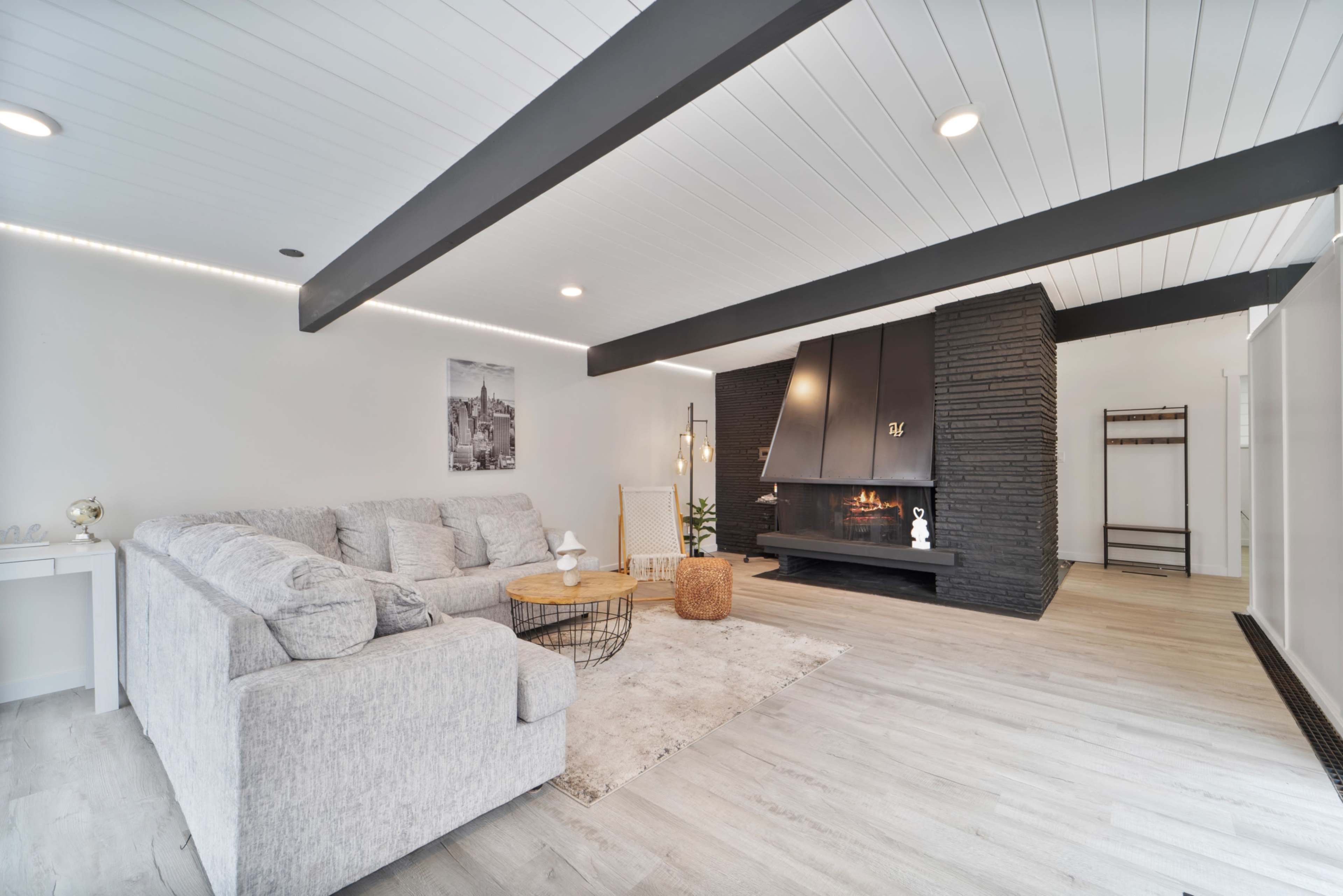 A modern living room with a gray sectional sofa, a round wooden coffee table, and a black stone fireplace against a white wall.