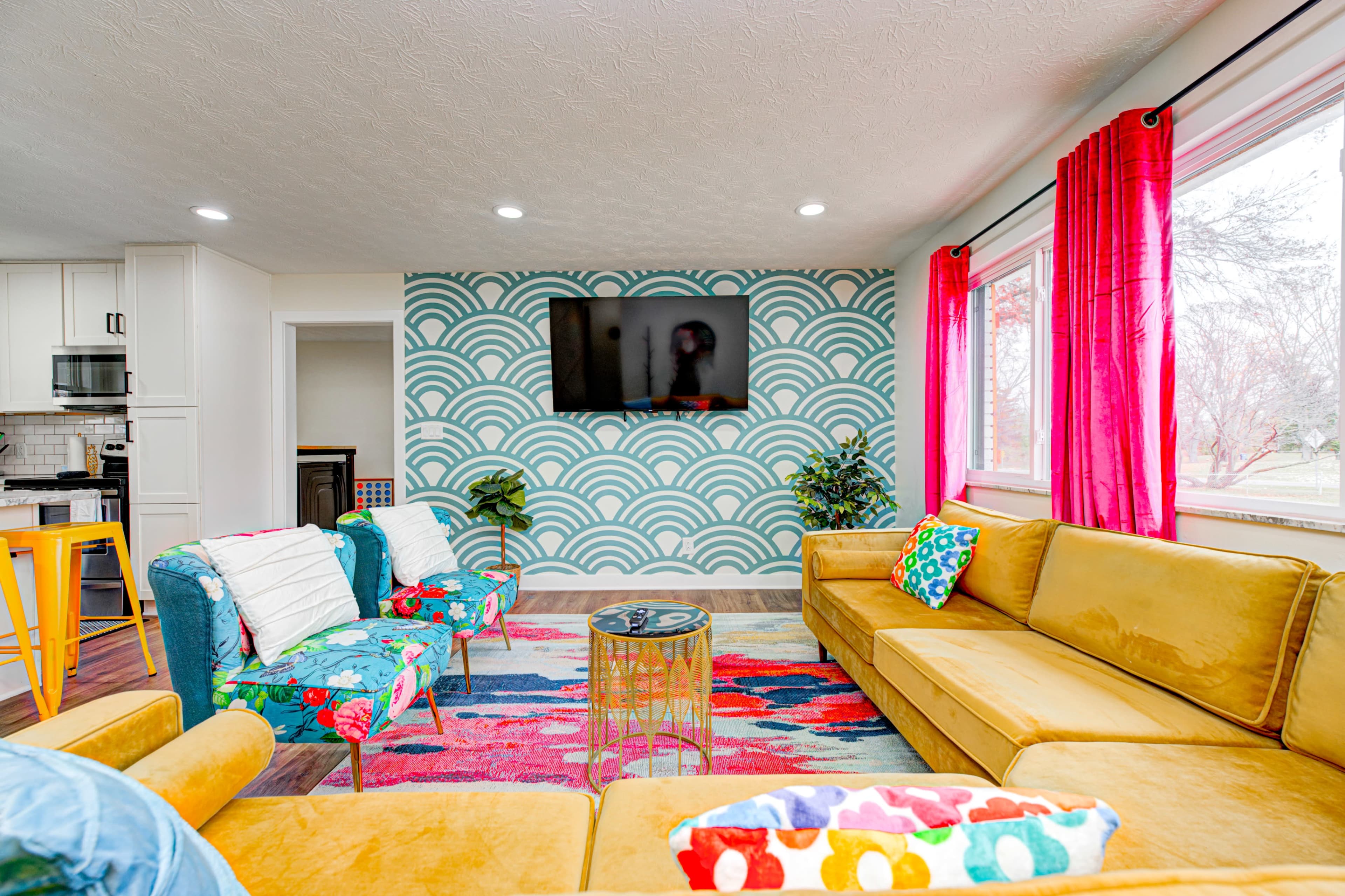 The living room features a vibrant design with colorful armchairs, a large yellow sofa, a patterned accent wall, and a flat-screen TV.
