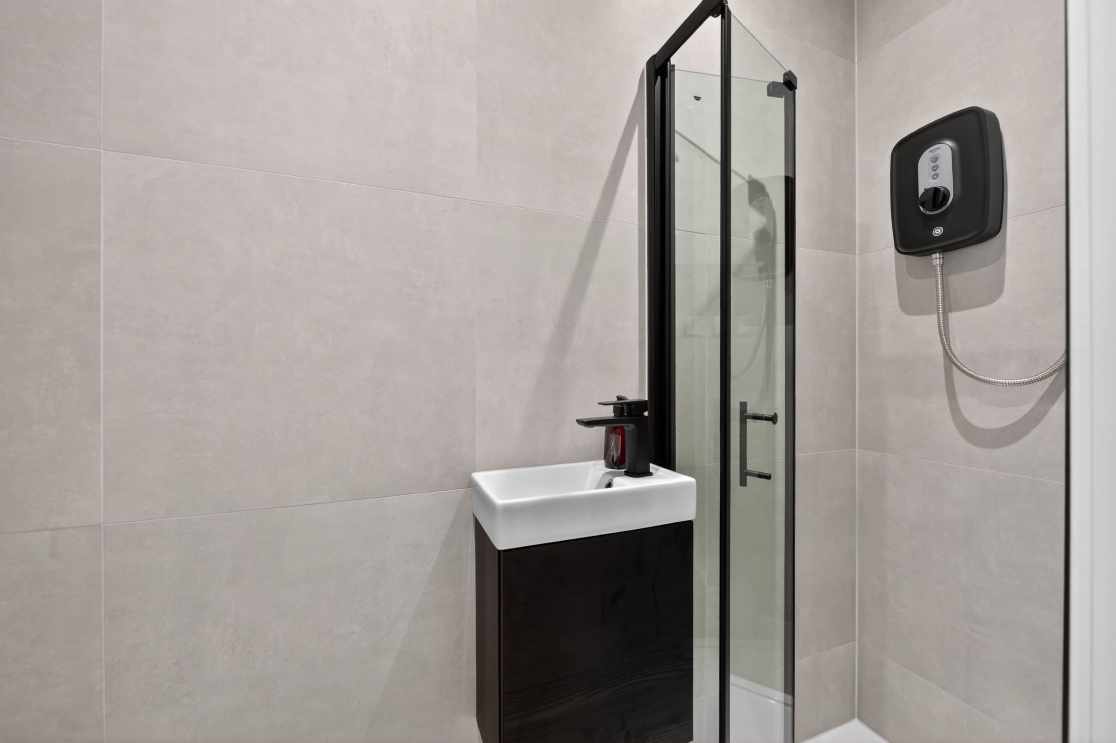 The image depicts a modern bathroom featuring a shower enclosure, a wall-mounted soap dispenser, and sleek tile walls.