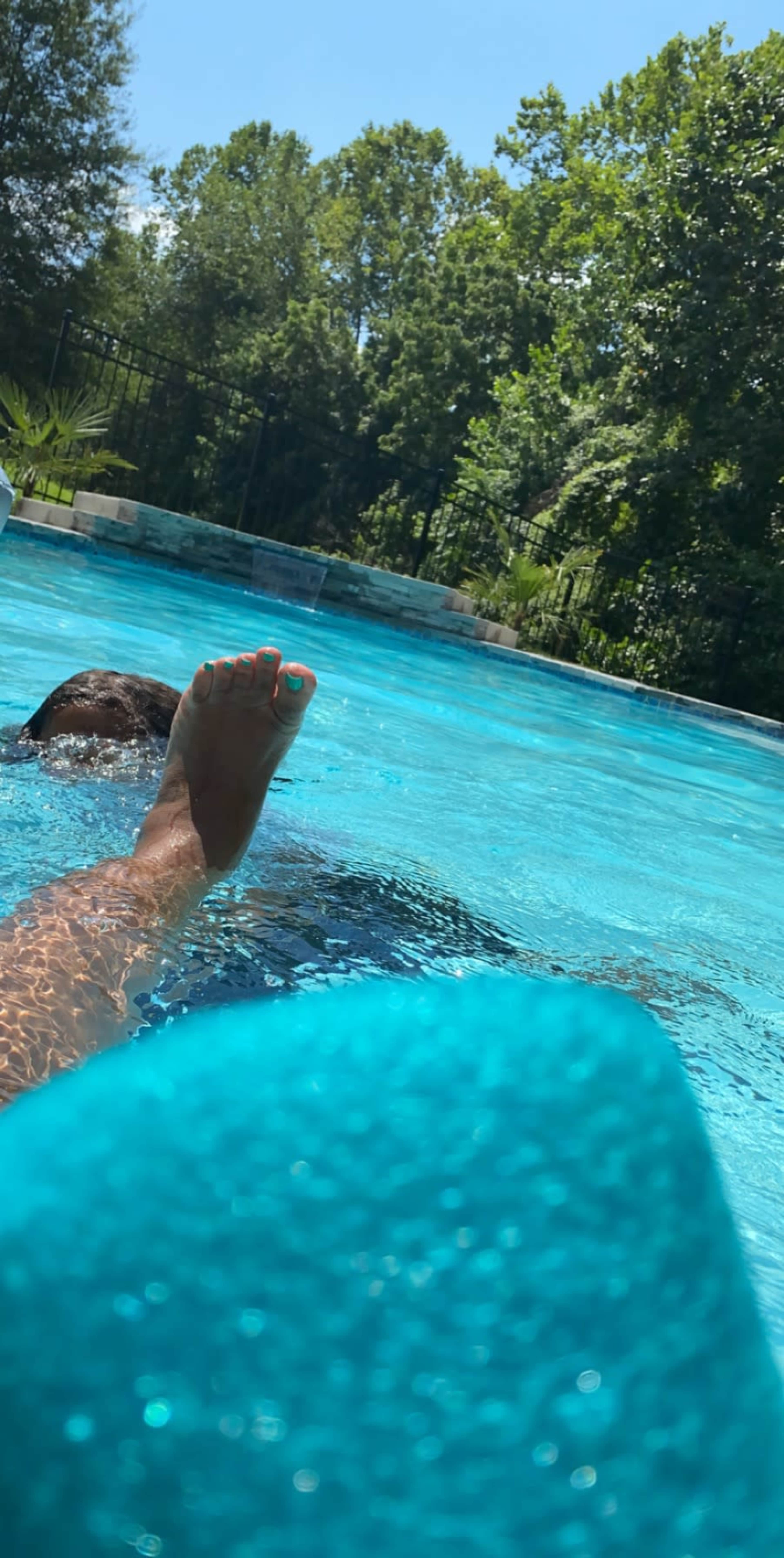 A person is relaxing in a swimming pool while partially submerged, with their foot visible above the water's surface.