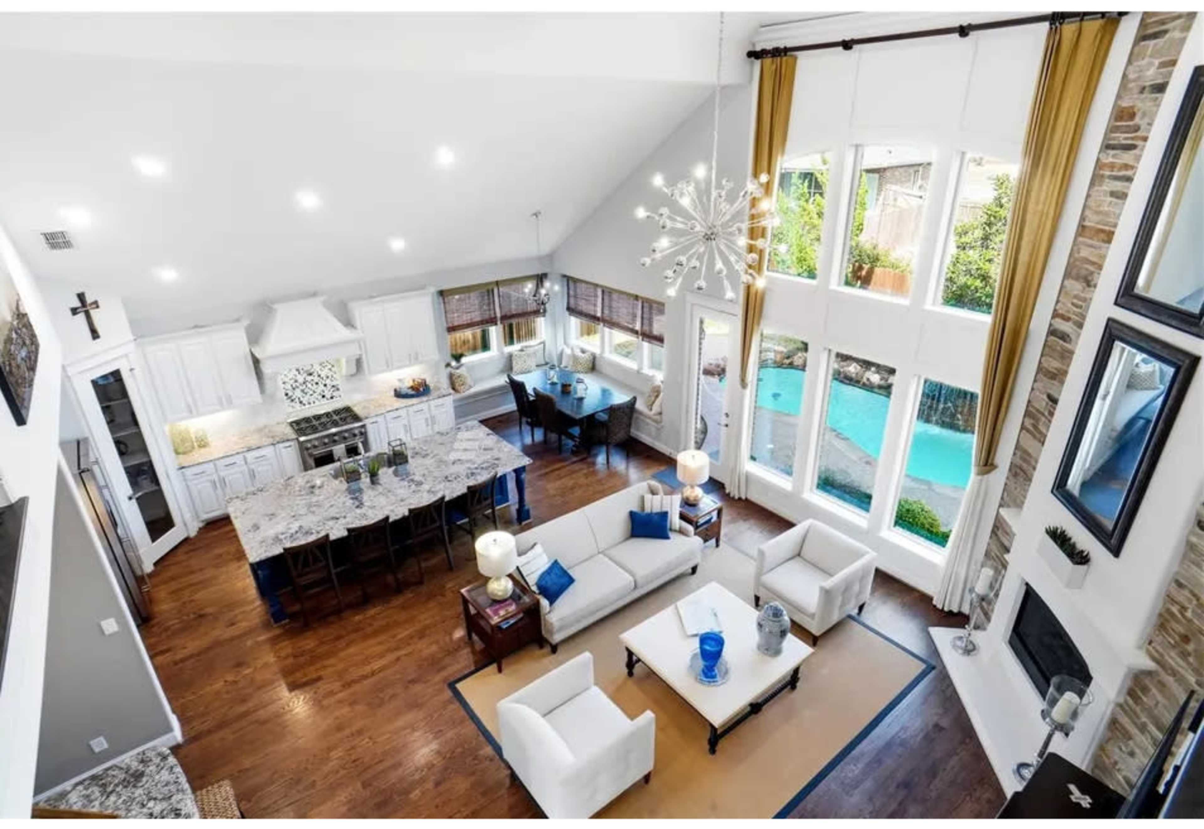 The image shows a spacious, modern living area and kitchen with large windows overlooking a pool and garden.