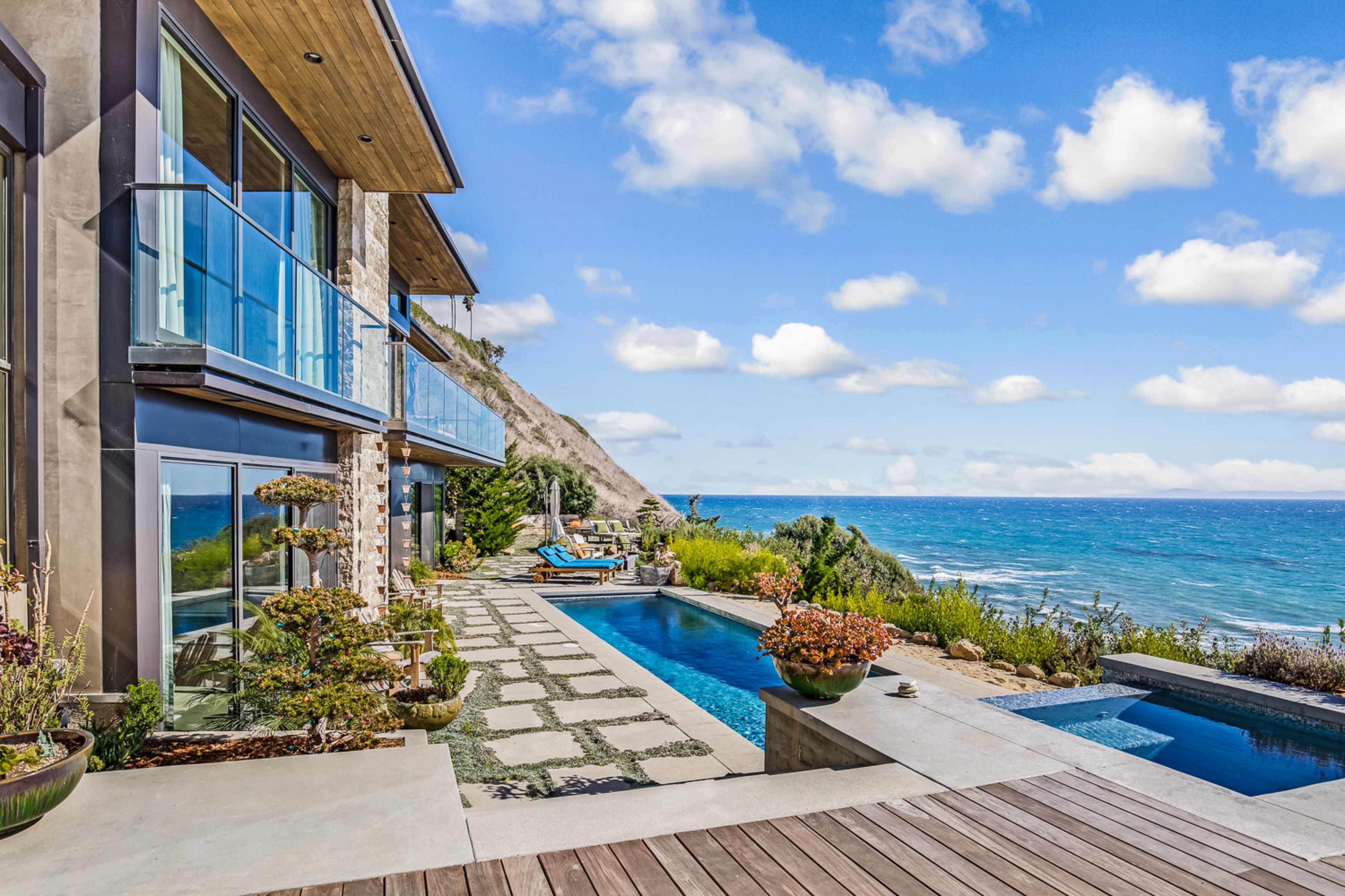 A modern seaside home features a terrace with a pool, landscaped pathways, and ocean views.