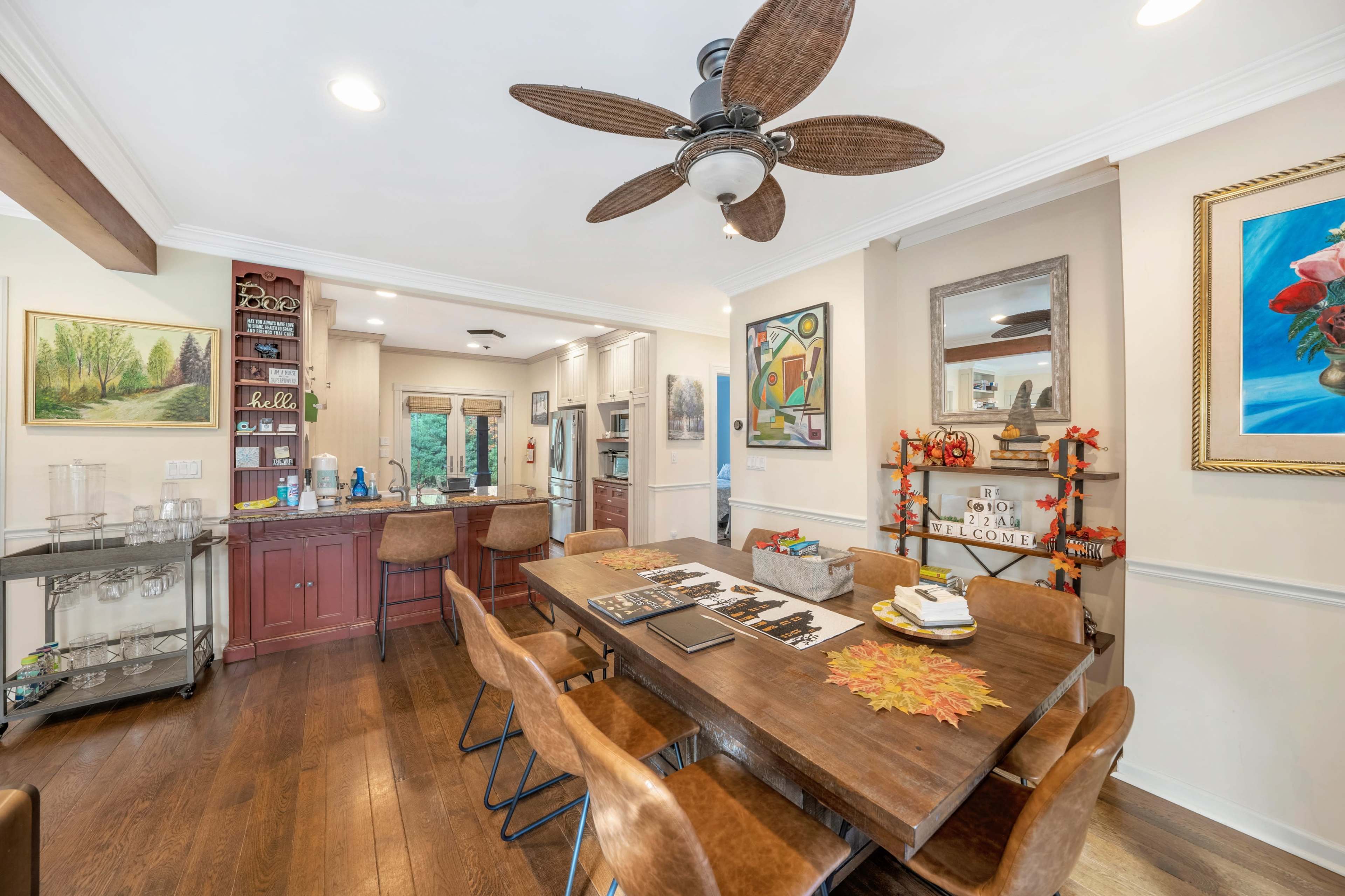 A warm and inviting kitchen and dining area featuring a large wooden table surrounded by chairs, a ceiling fan, and decorative wall art.