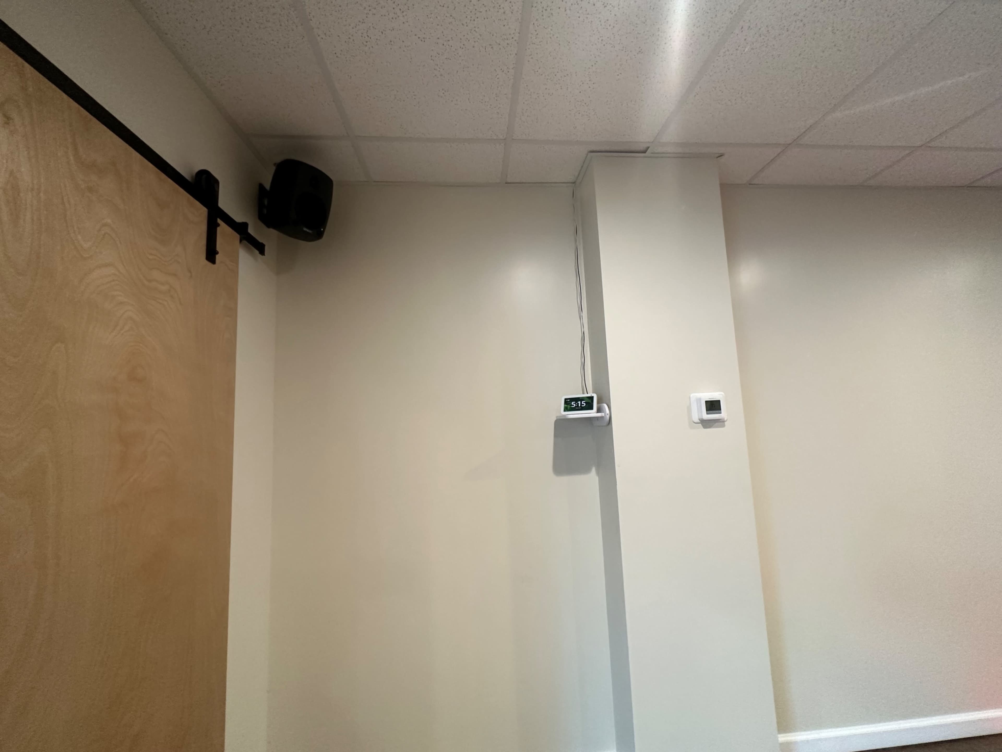 A corner of a room with a wooden sliding door, a wall-mounted clock, and a ventilation unit on the ceiling.