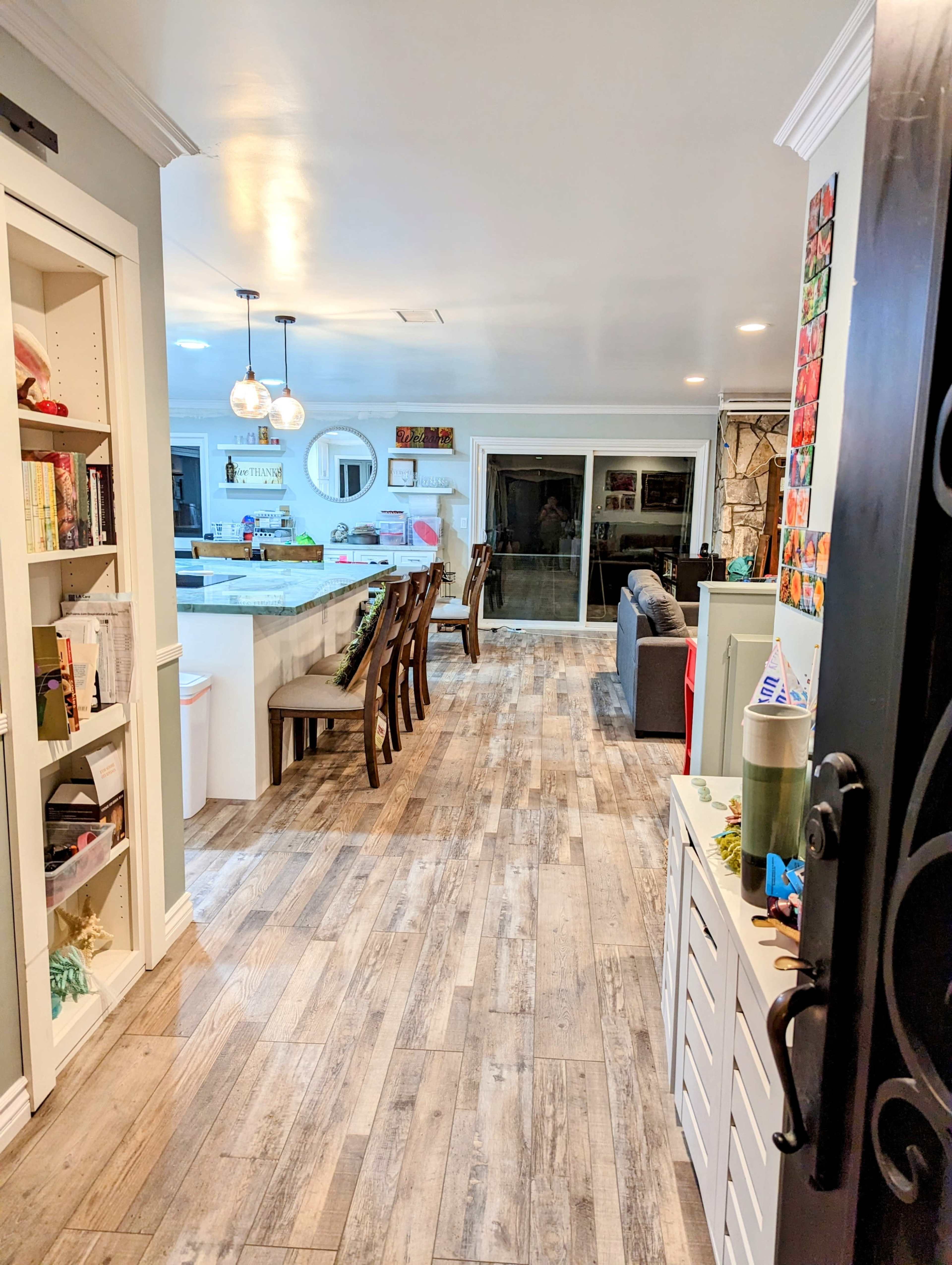 A well-lit hallway leads to an open kitchen and living area, featuring wooden flooring and a combination of bookshelves and seating.
