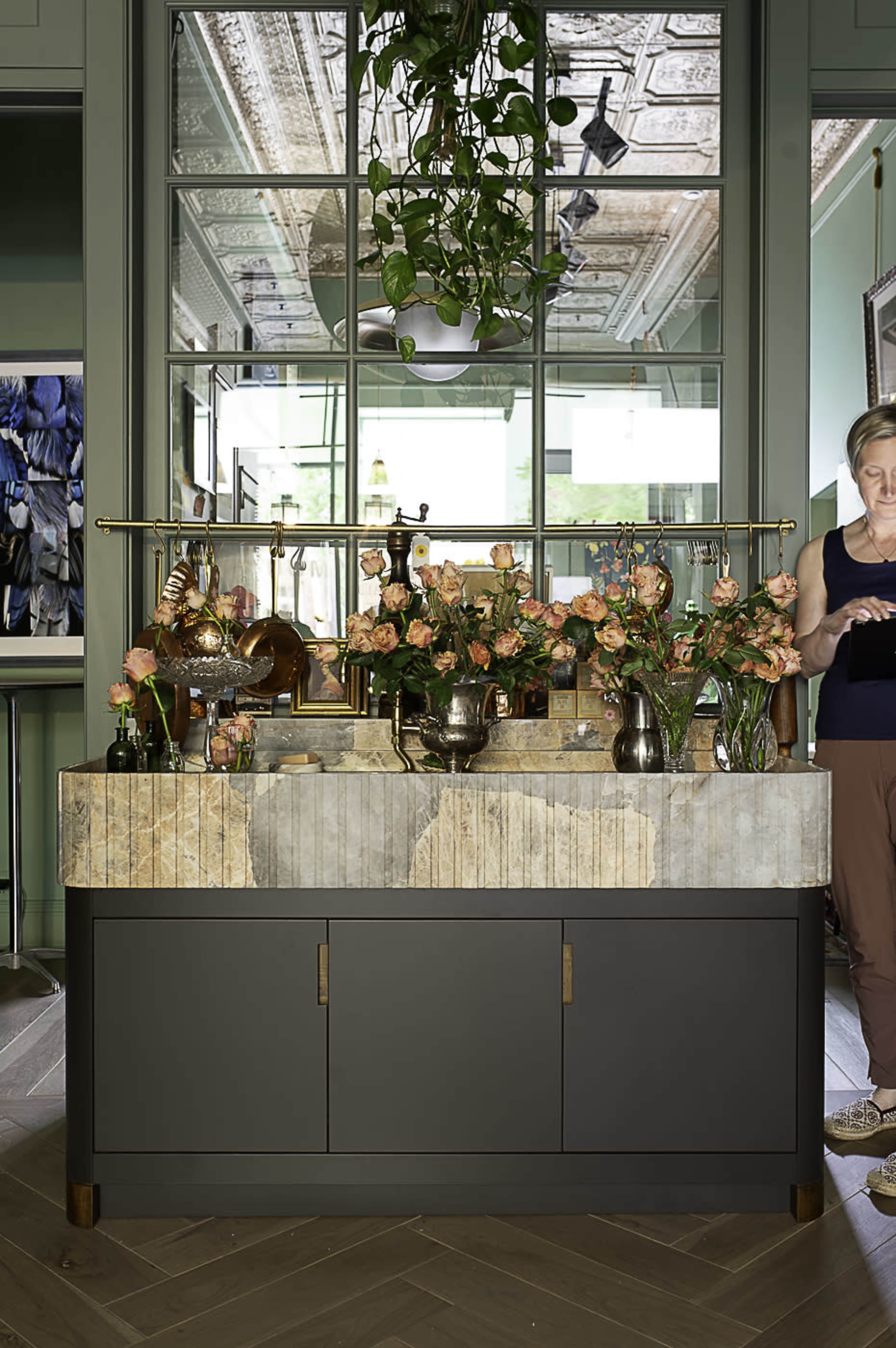 A modern countertop with a mix of floral arrangements and decorative items is set against a backdrop of mirrors and green walls.