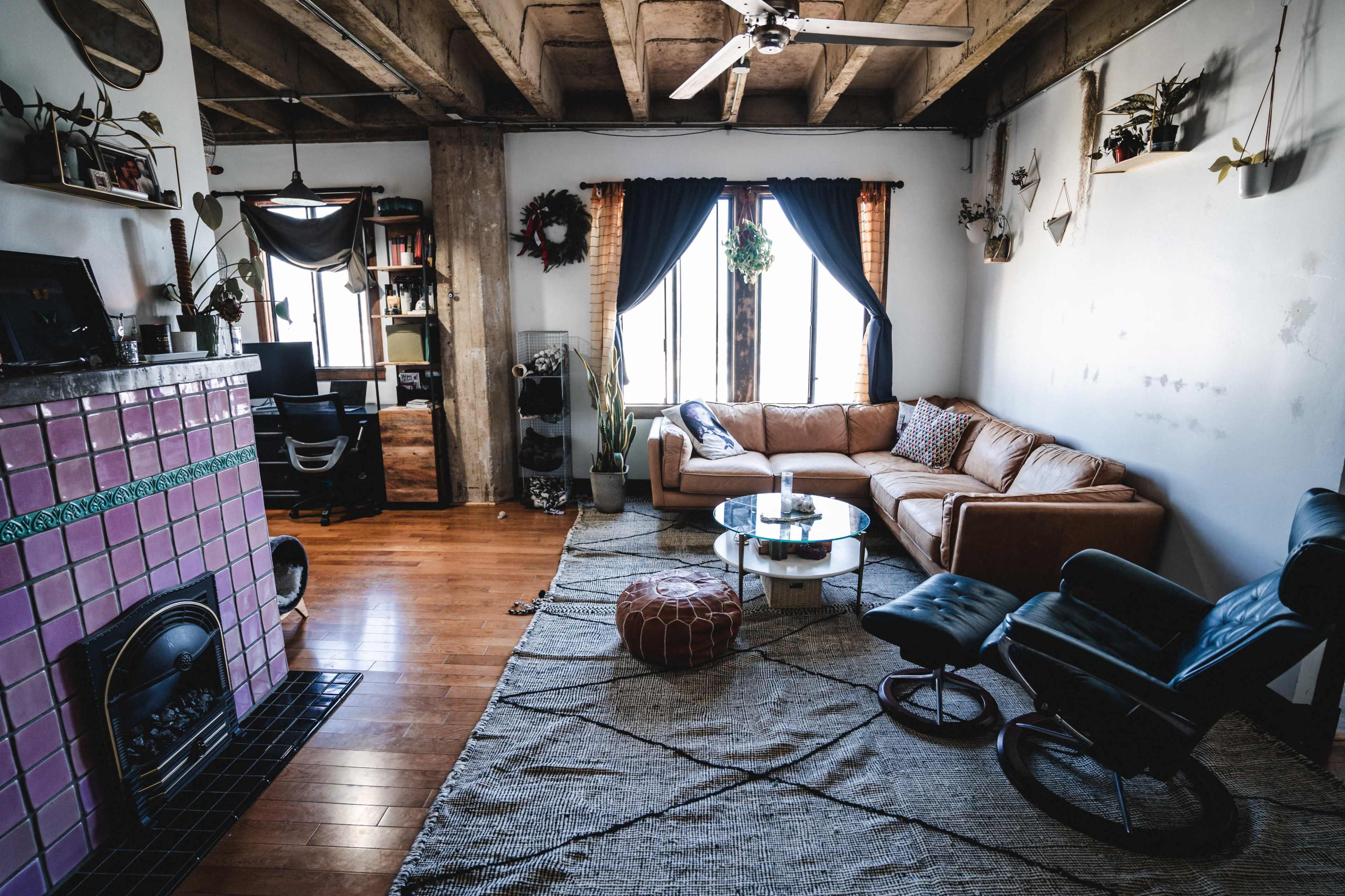 The image shows a modern living room with a brown sofa, a glass coffee table, a patterned rug, and a brick fireplace.