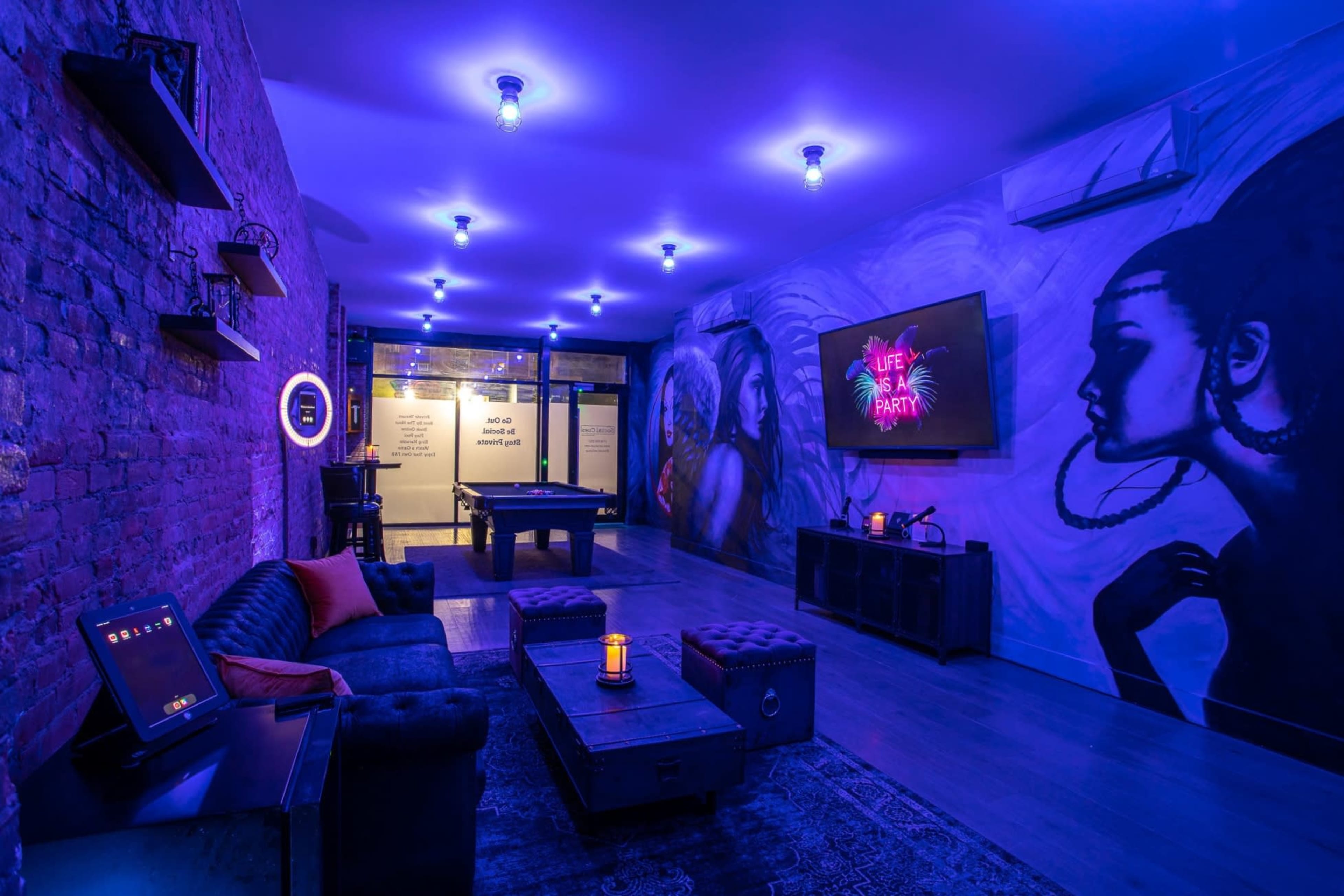The room features purple lighting, a mural on the wall, a billiards table, and seating with a coffee table, creating a vibrant atmosphere.