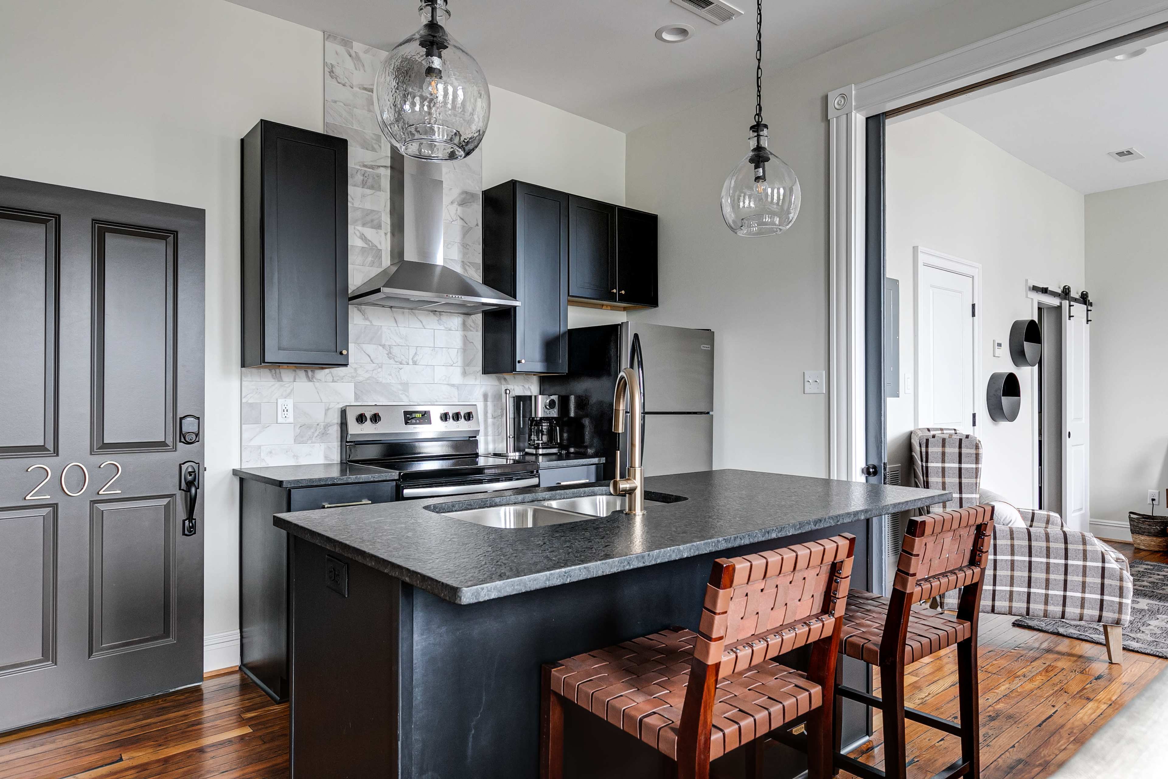 A modern kitchen featuring a black countertop, stainless steel appliances, and two wooden bar stools.