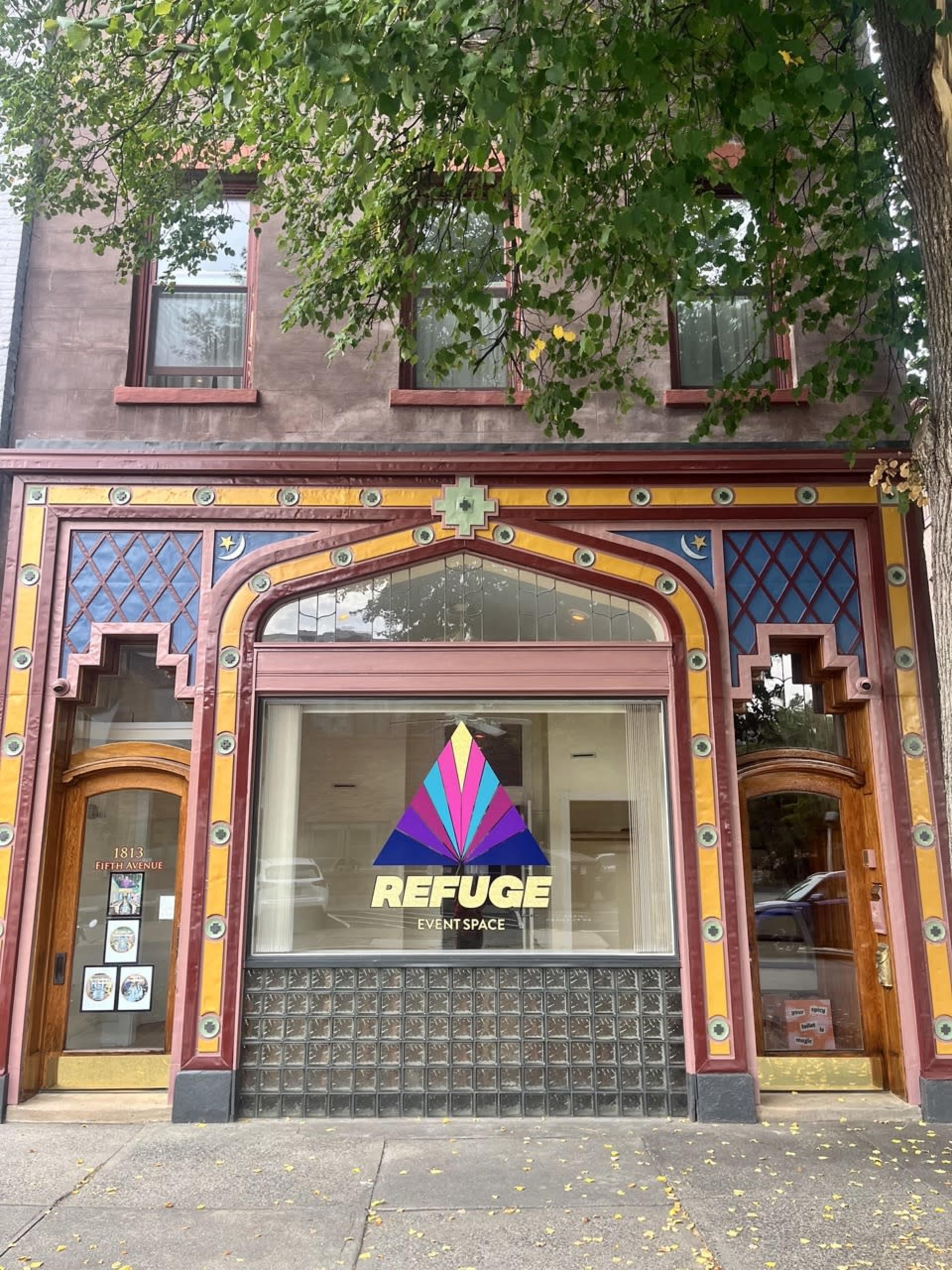 The front of a brightly colored building features an ornate facade with a large window displaying the words "REFUGE EVENT SPACE."