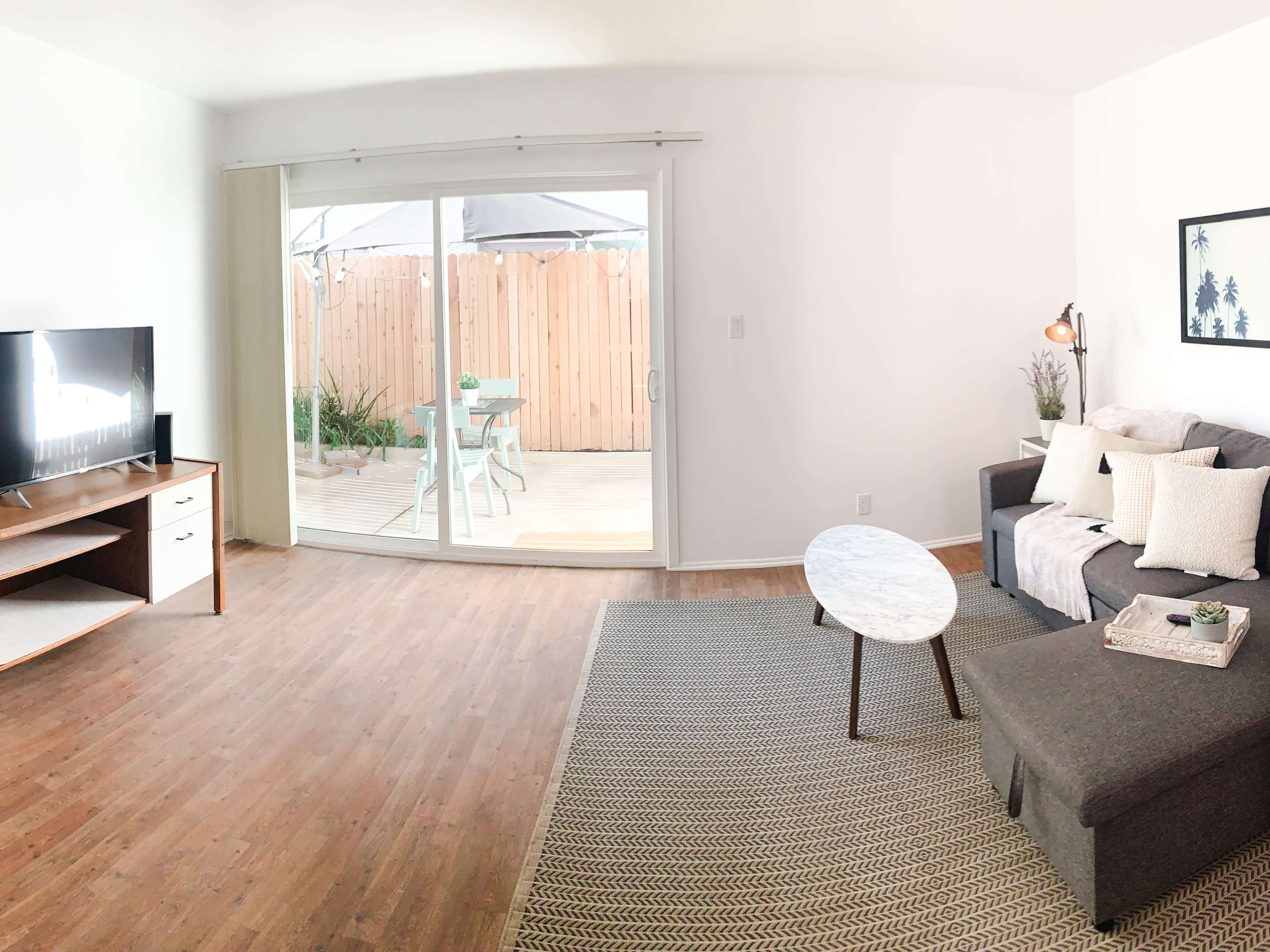 A modern living room with a gray sectional sofa, a round marble coffee table, a television on a wooden stand, and large sliding doors that open to a deck area.