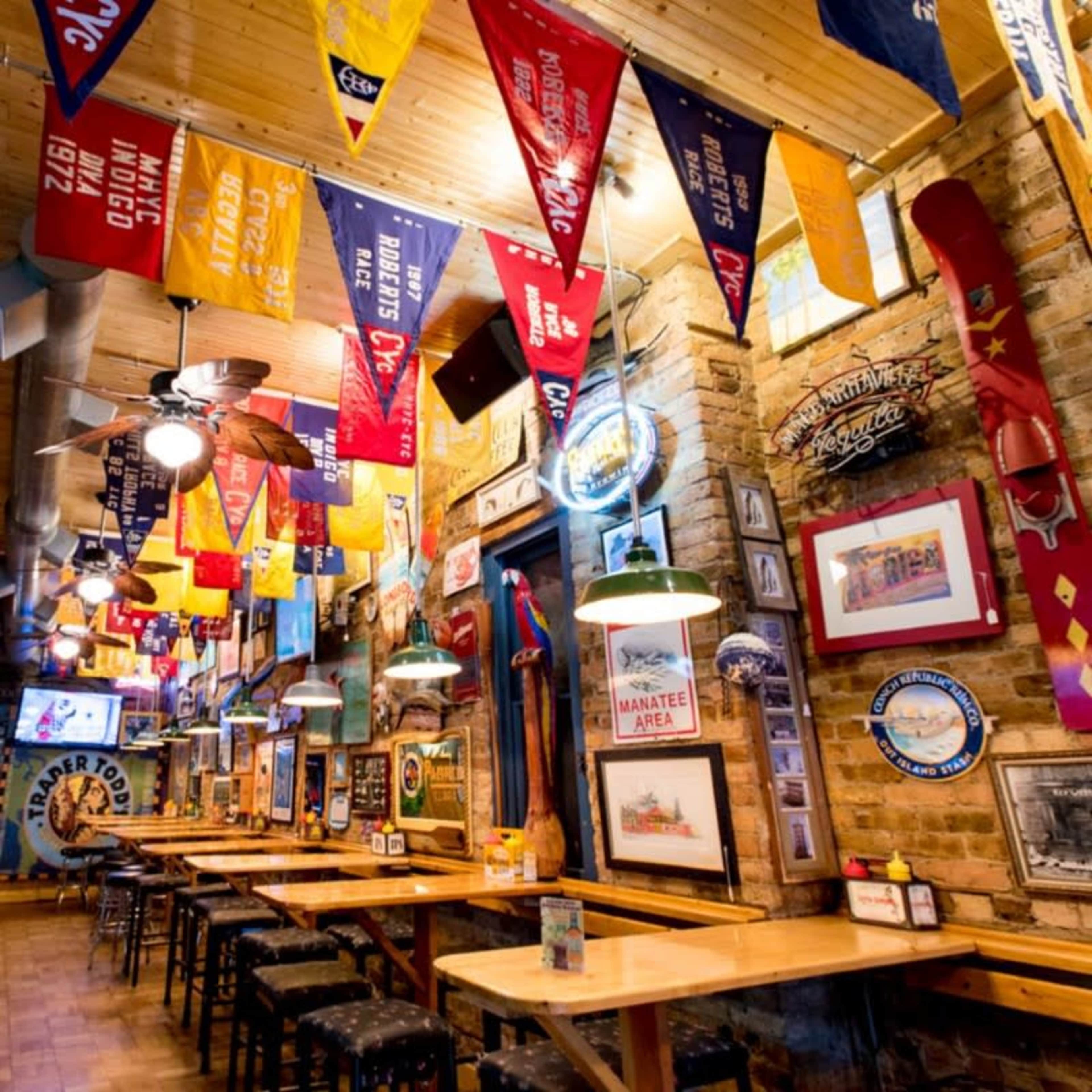 The image shows an indoor dining area of a restaurant decorated with colorful banners and memorabilia, featuring wooden tables and chairs under a wooden ceiling.