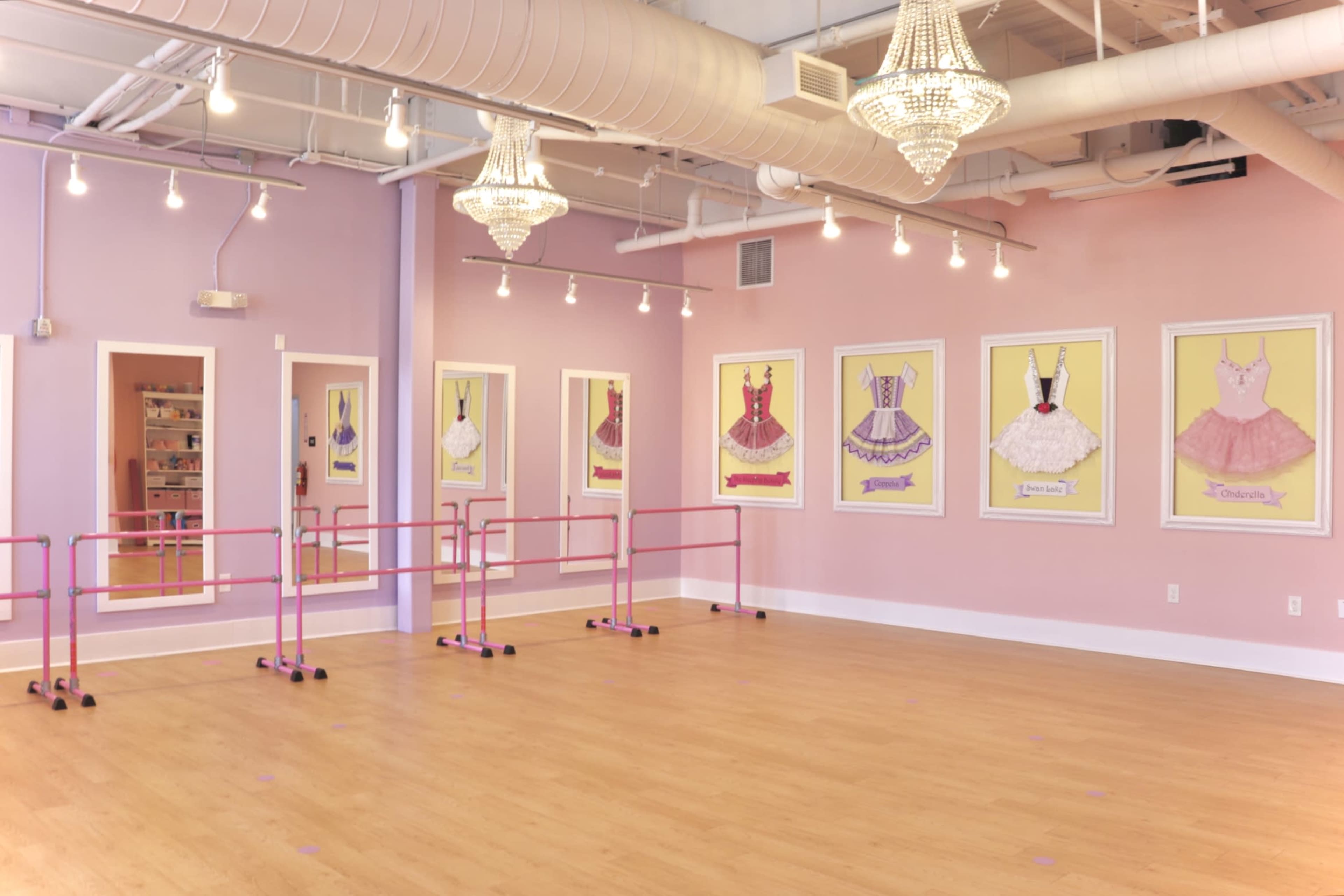 The image shows a dance studio with pink ballet barres, pastel-colored walls, and framed illustrations of dresses hung on the walls under decorative light fixtures.