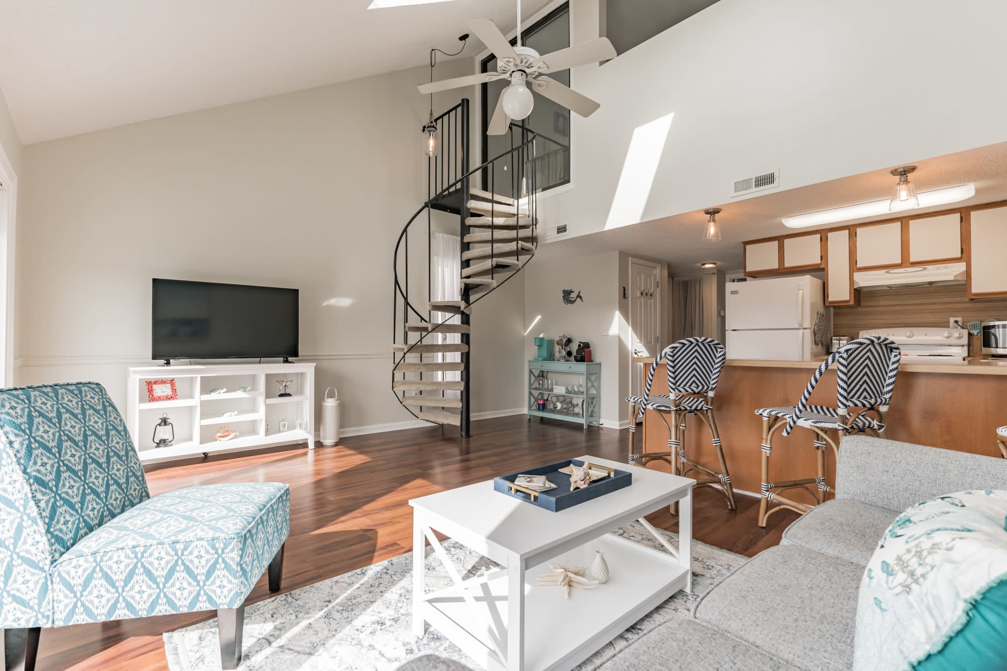 A bright living room with a spiral staircase, a television, and a kitchen area in an open layout.