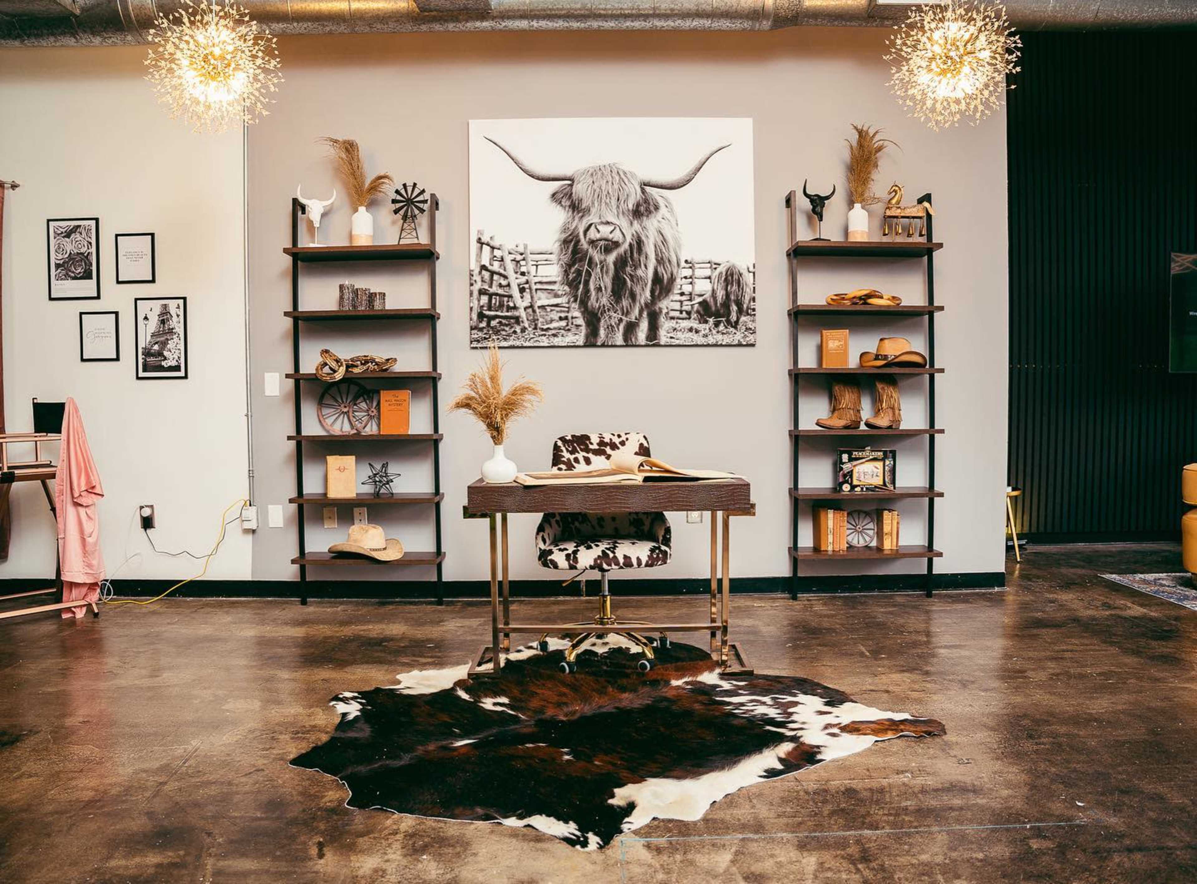 A modern office space features a wooden desk with a stylish chair, a large bull photograph on the wall, and open shelves displaying various decor items.