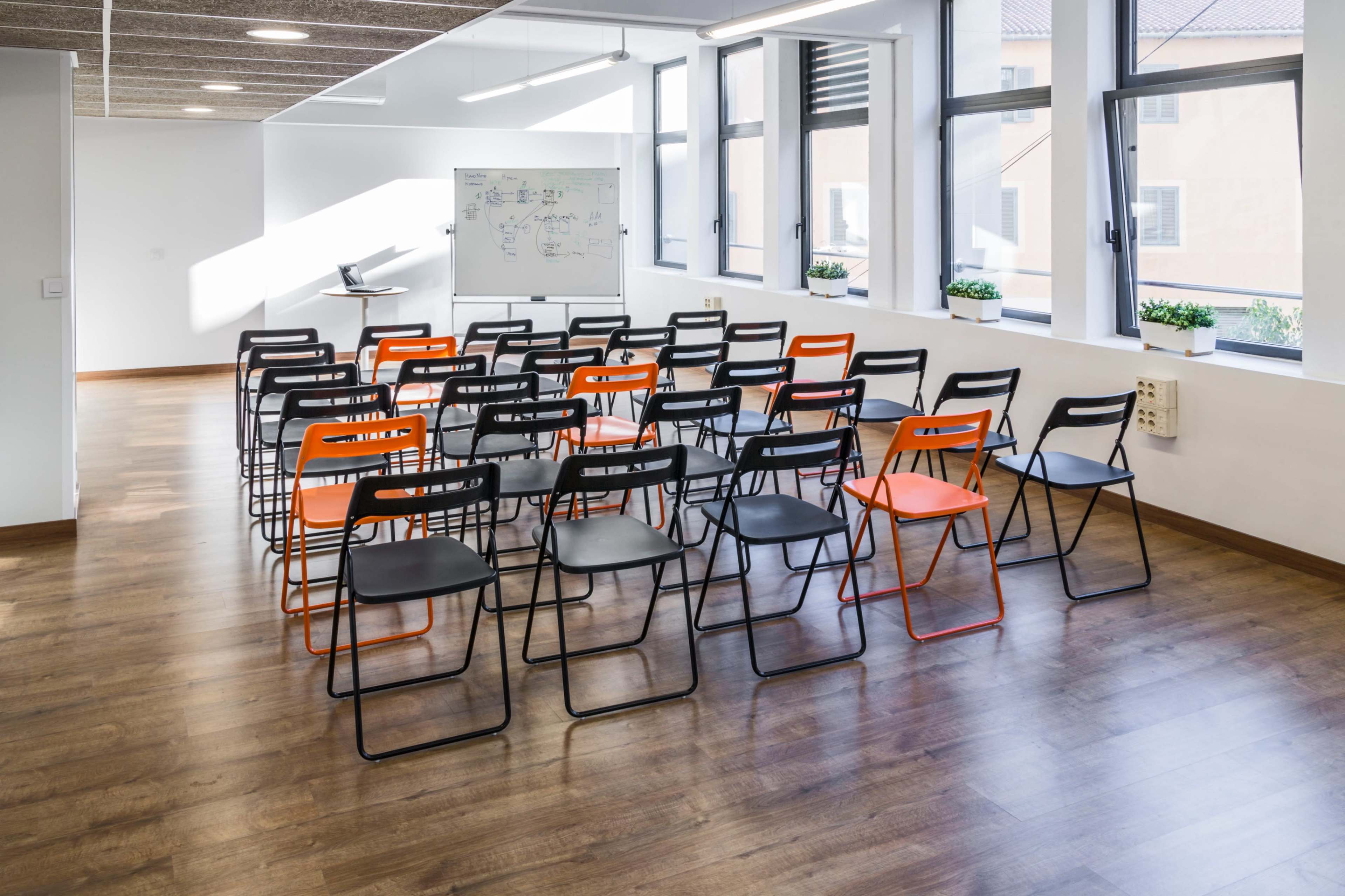 A row of black and orange chairs is arranged facing a whiteboard in a well-lit classroom.
