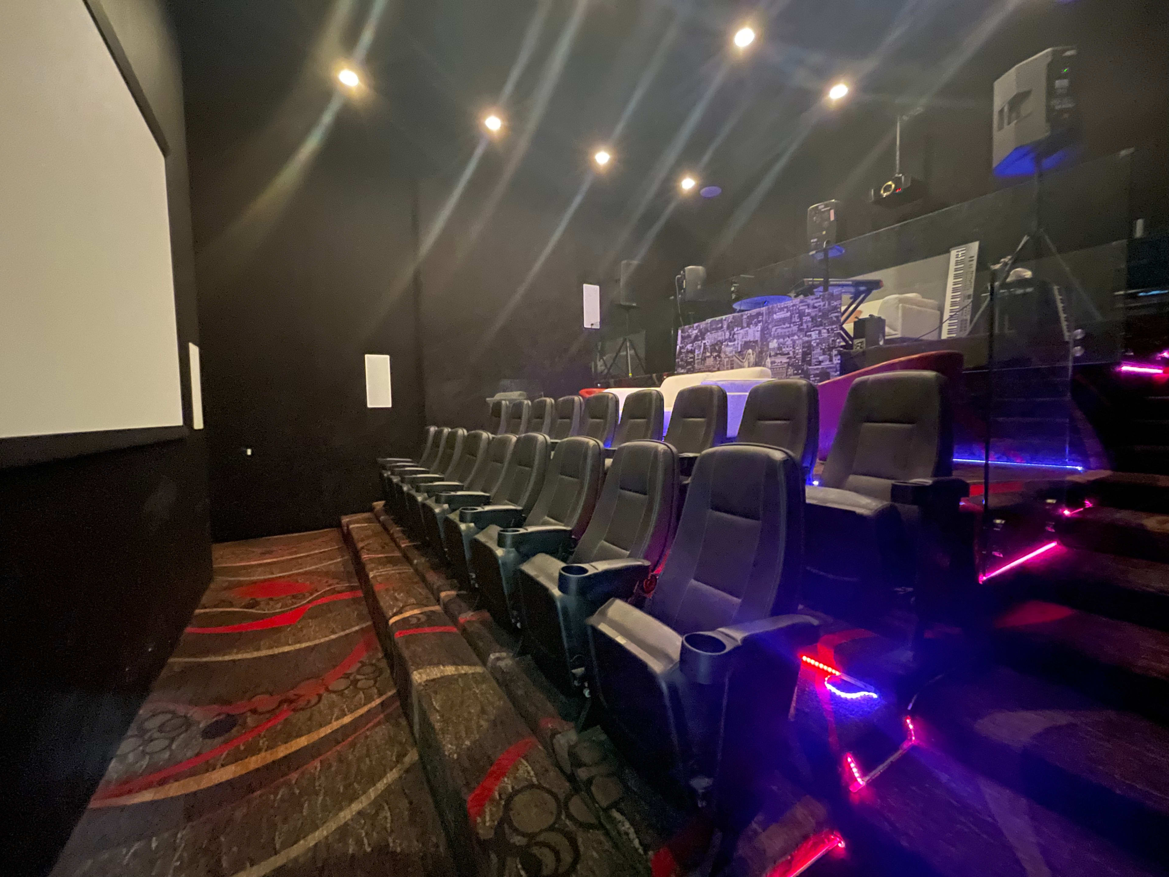A row of empty theater seats in a dimly lit cinema with a stage in the background.