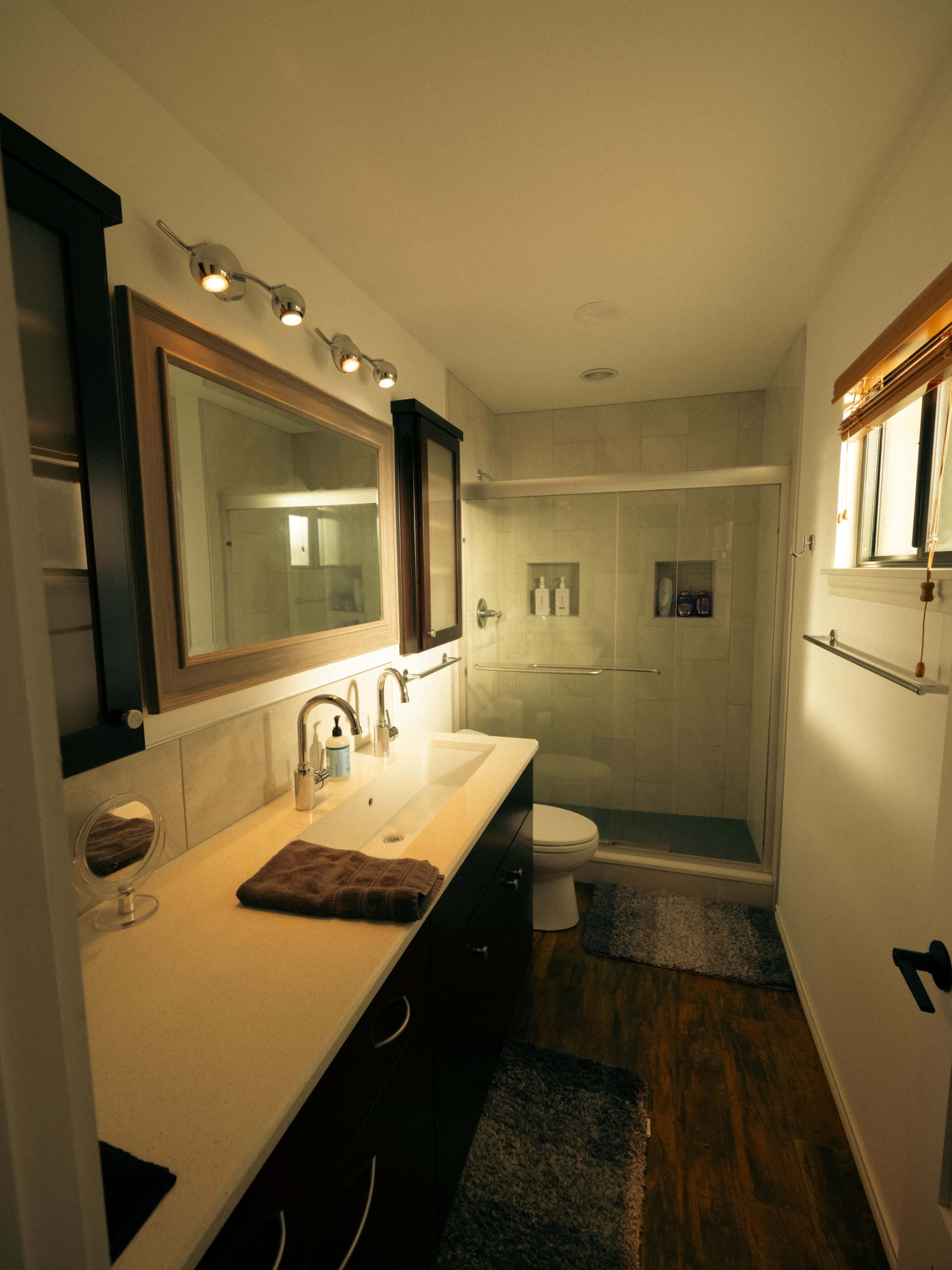 The image shows a modern bathroom featuring a sink with a countertop, a mirror, a shower enclosure, and a toilet.