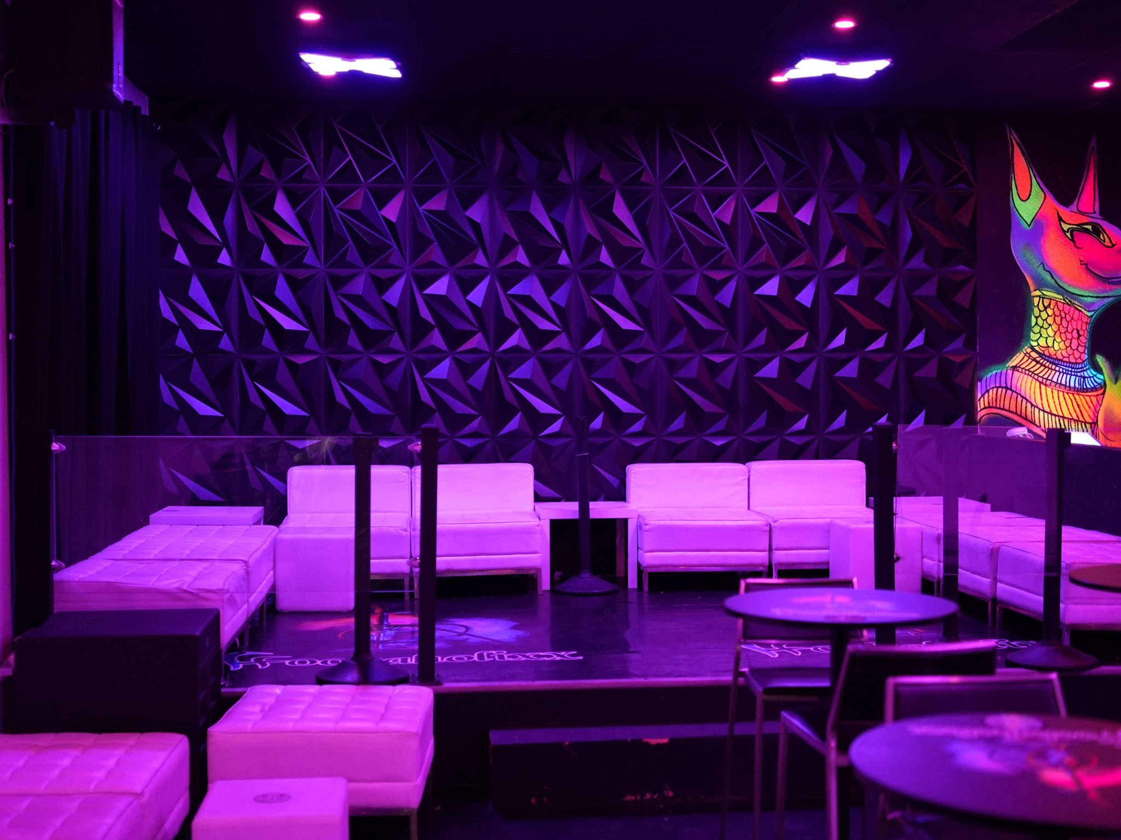 A lounge area with white seating and a colorful wall mural in a dimly lit setting.