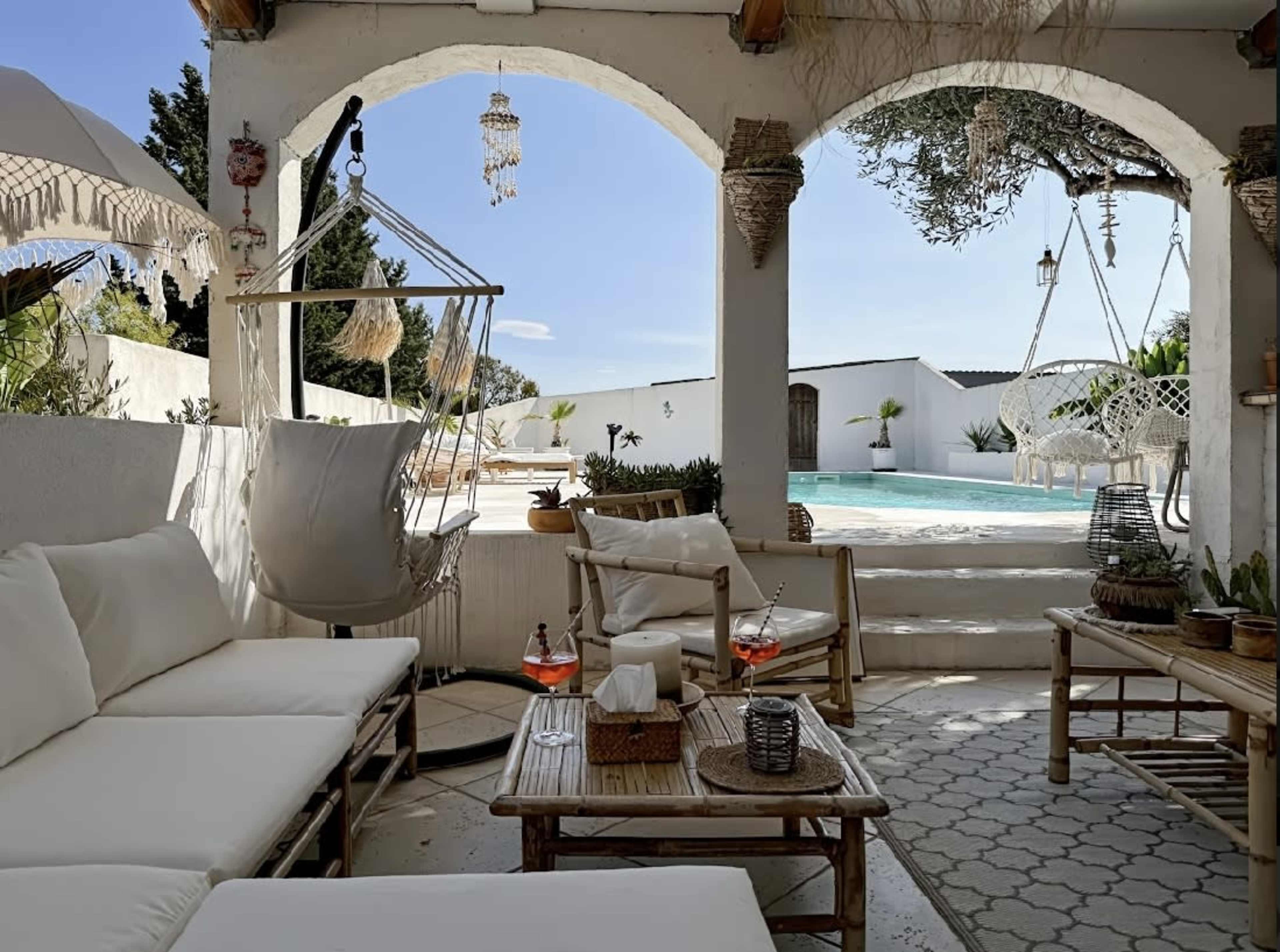 A cozy outdoor seating area features a hanging chair and a view of a swimming pool surrounded by greenery.