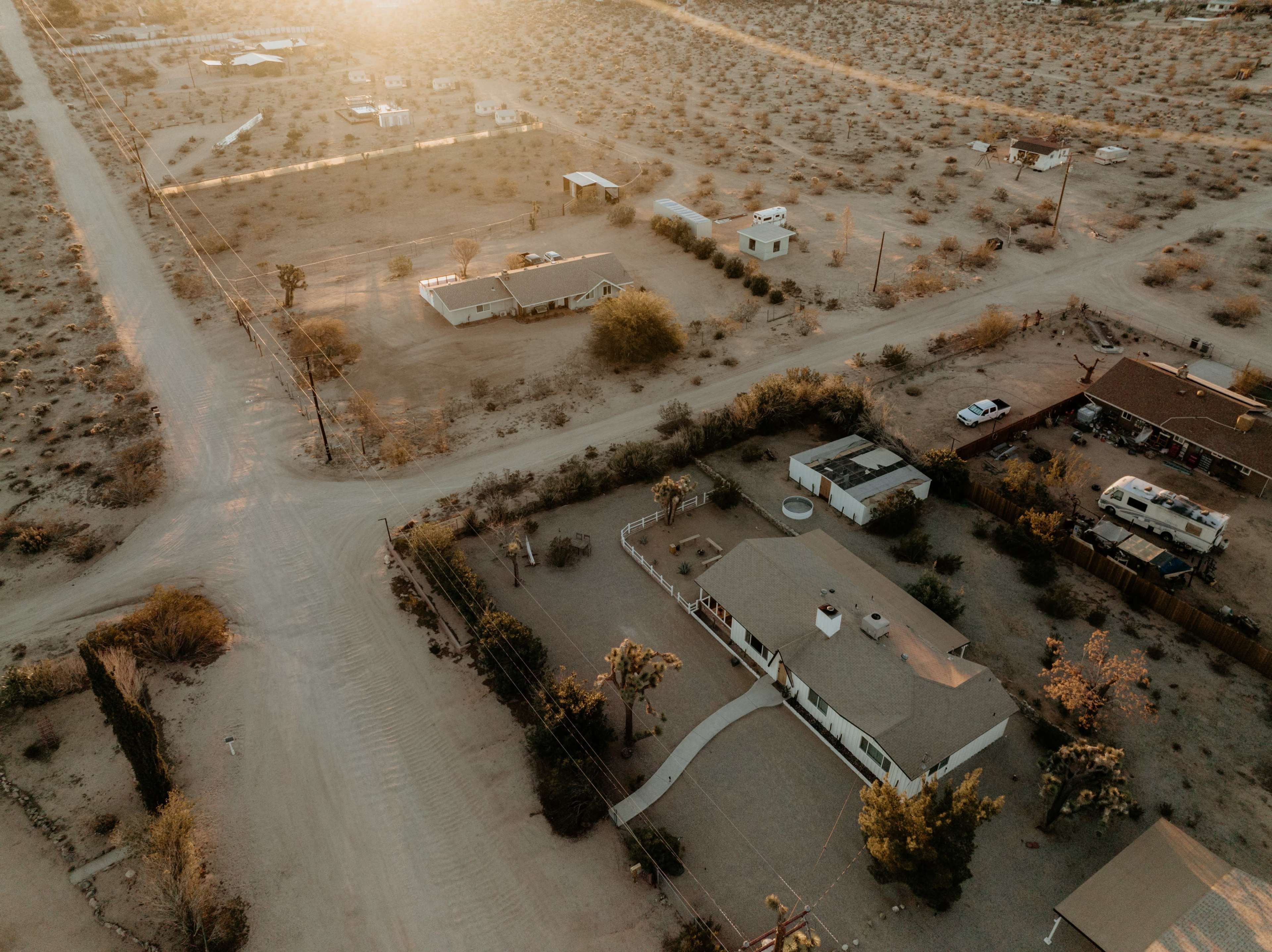 A desert landscape with scattered homes and dirt roads intersecting under a warm sunset.
