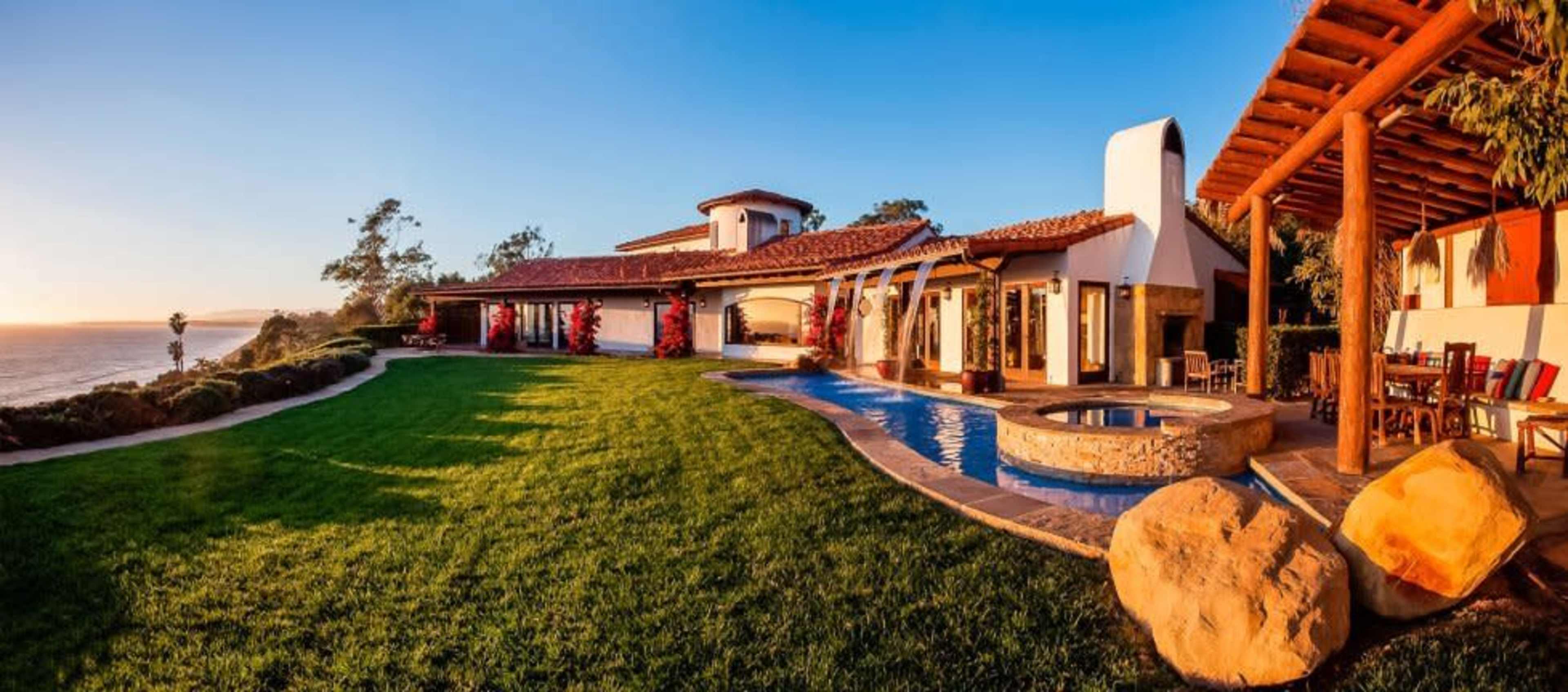 A large coastal villa features a pool, landscaped lawn, and ocean views.
