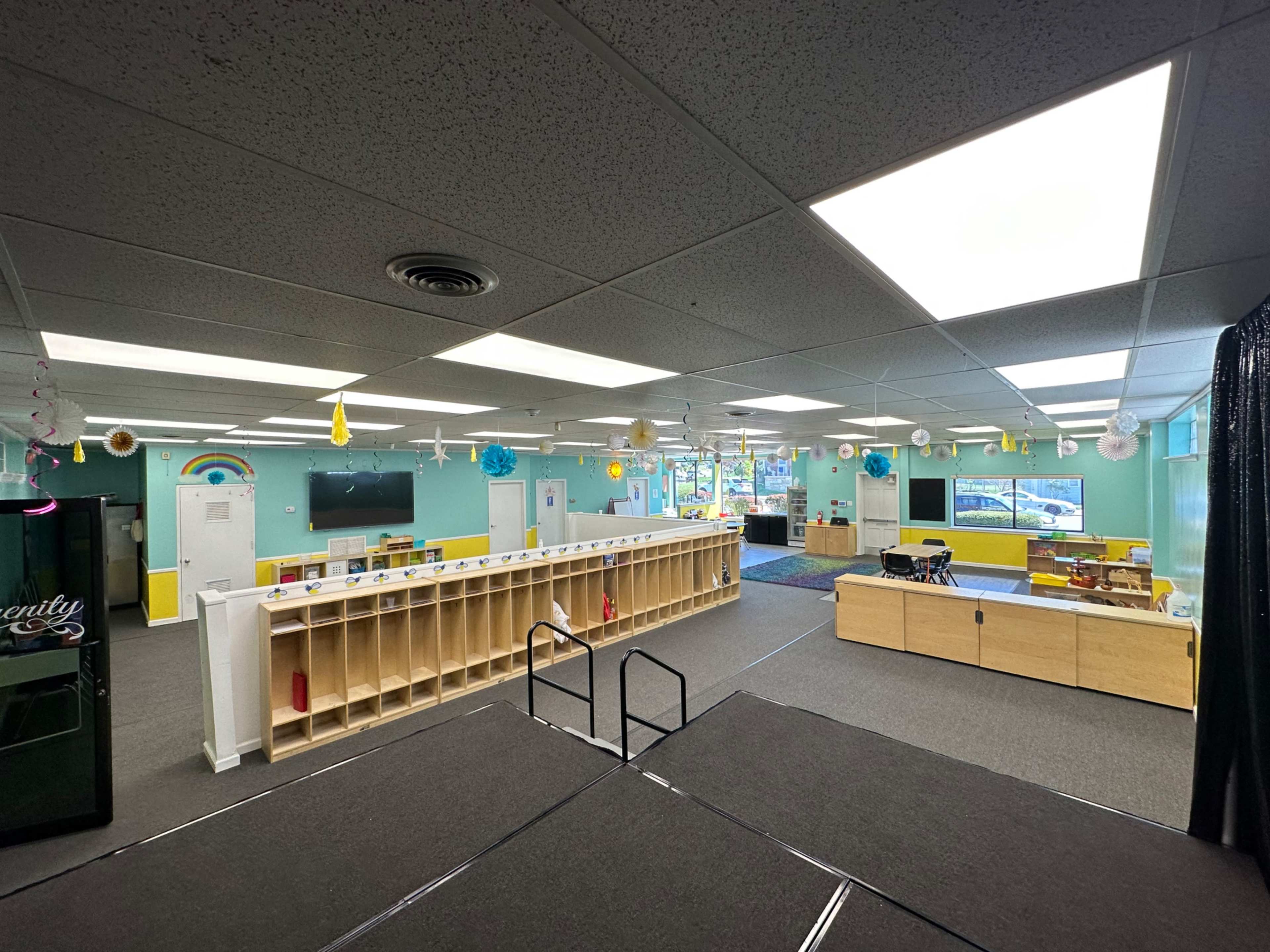 A brightly lit preschool classroom with organized storage shelves and various play areas.