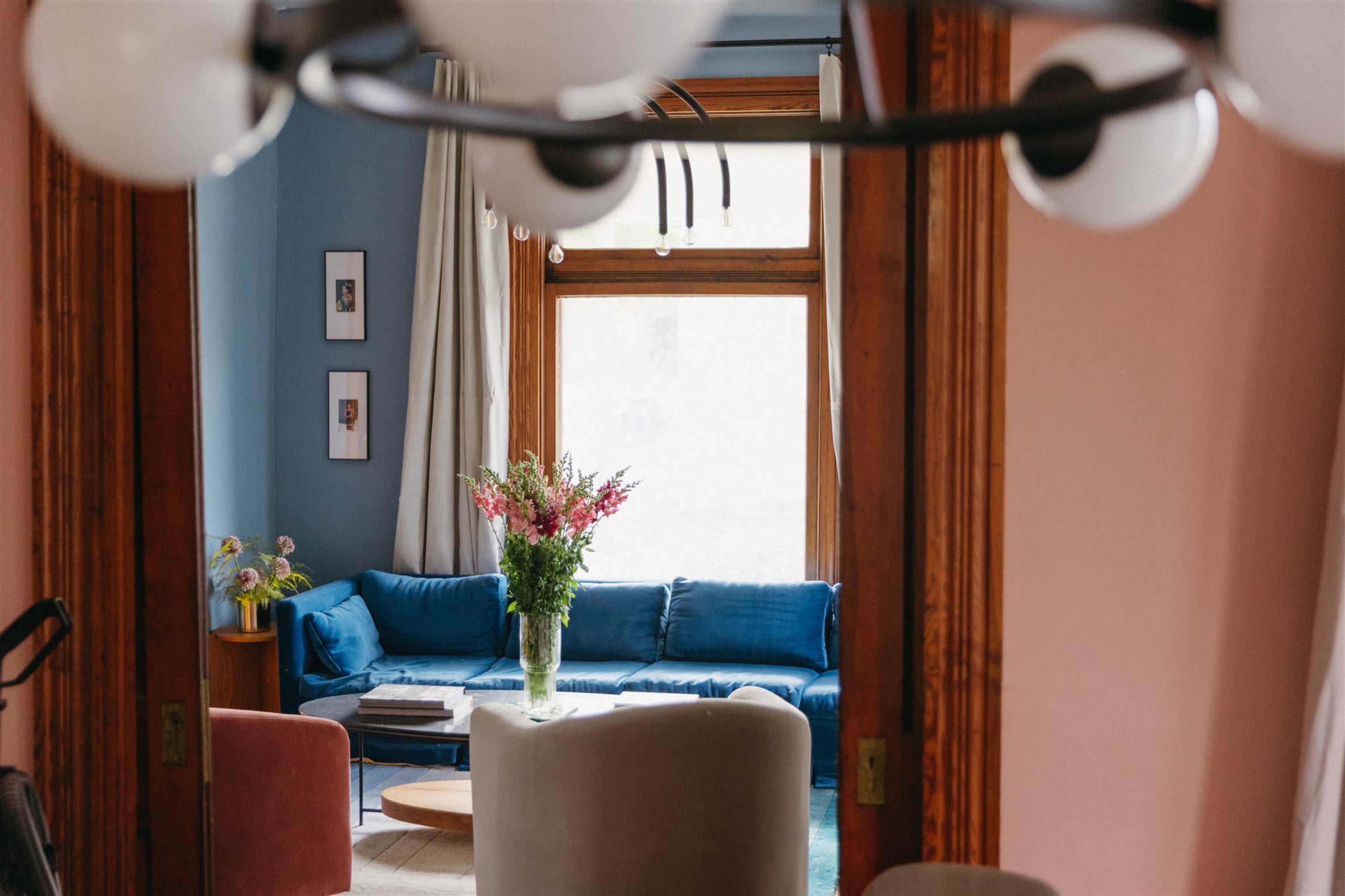 A living room features a blue sofa with a coffee table and a vase of flowers, framed by two wooden doorways.