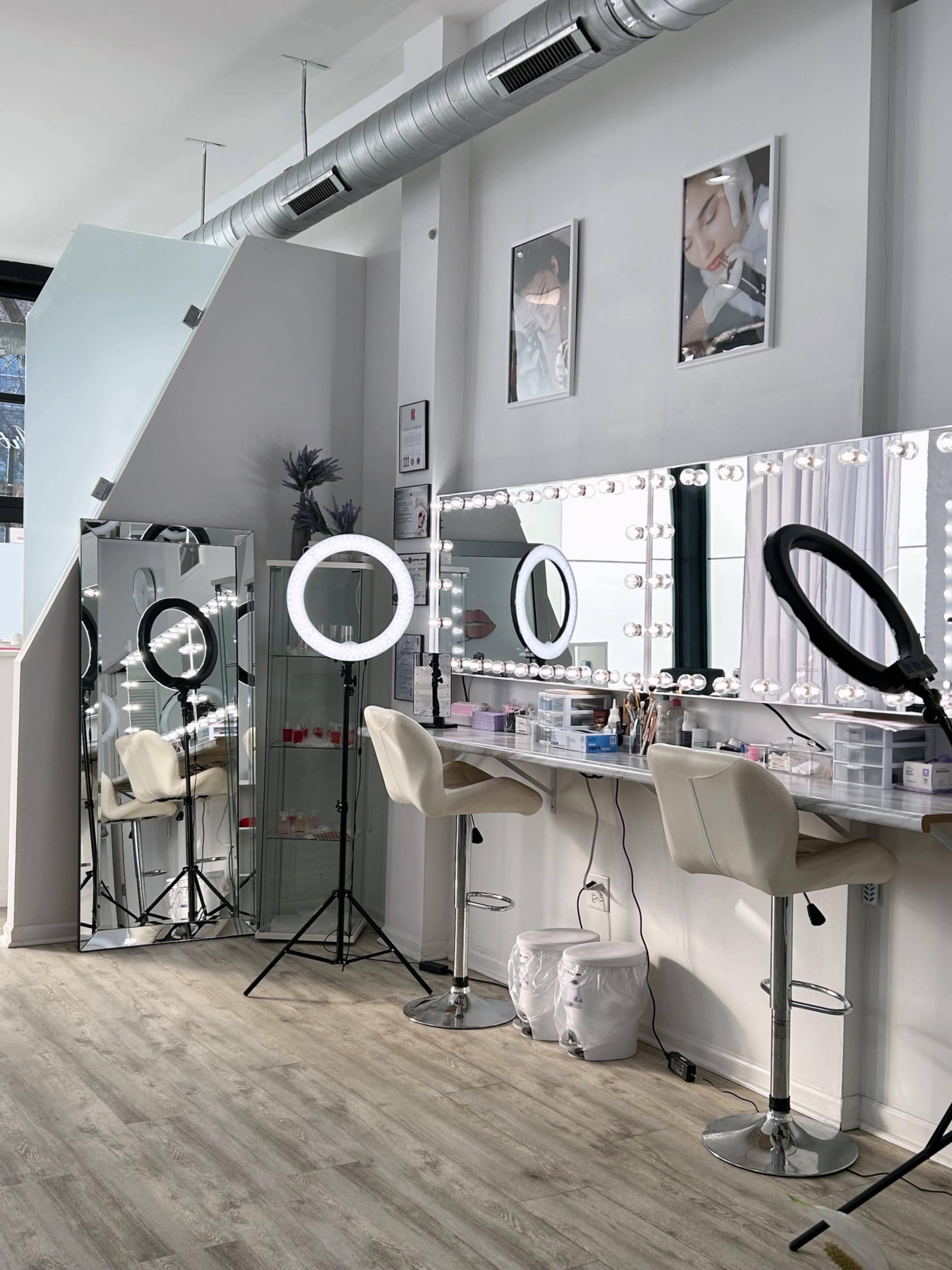A makeup studio featuring multiple mirrors, ring lights, and seating arrangements along with a large wall mirror.