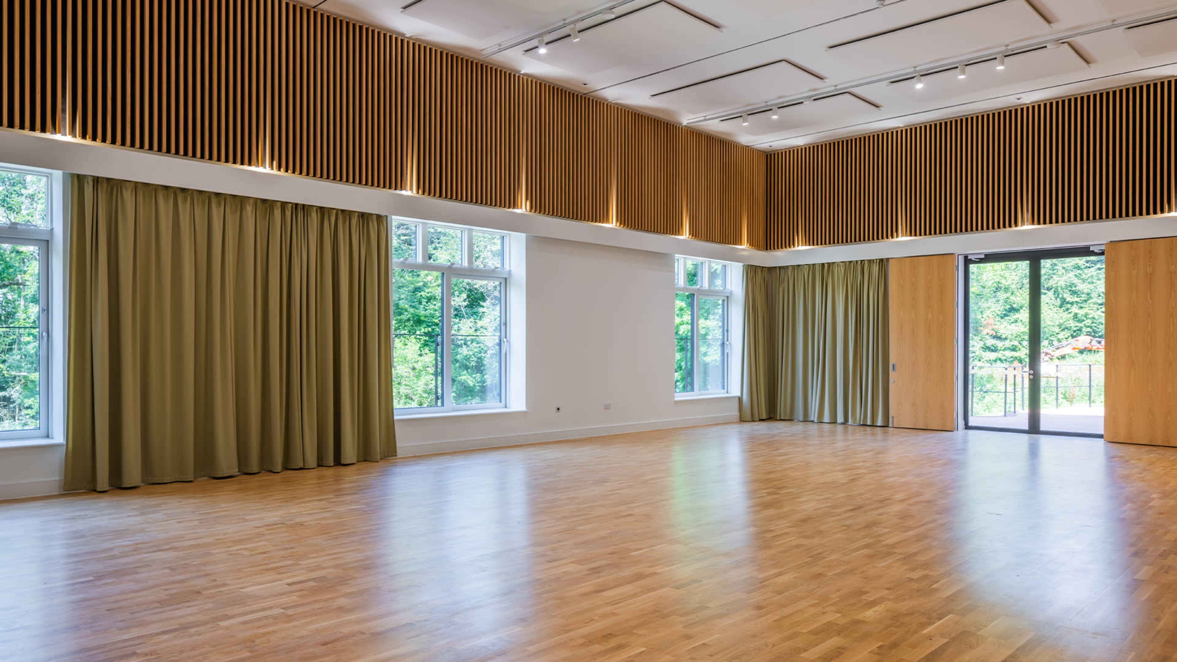 A spacious room with wooden floors, large windows, and curtains, featuring a wood-paneled wall at the top.