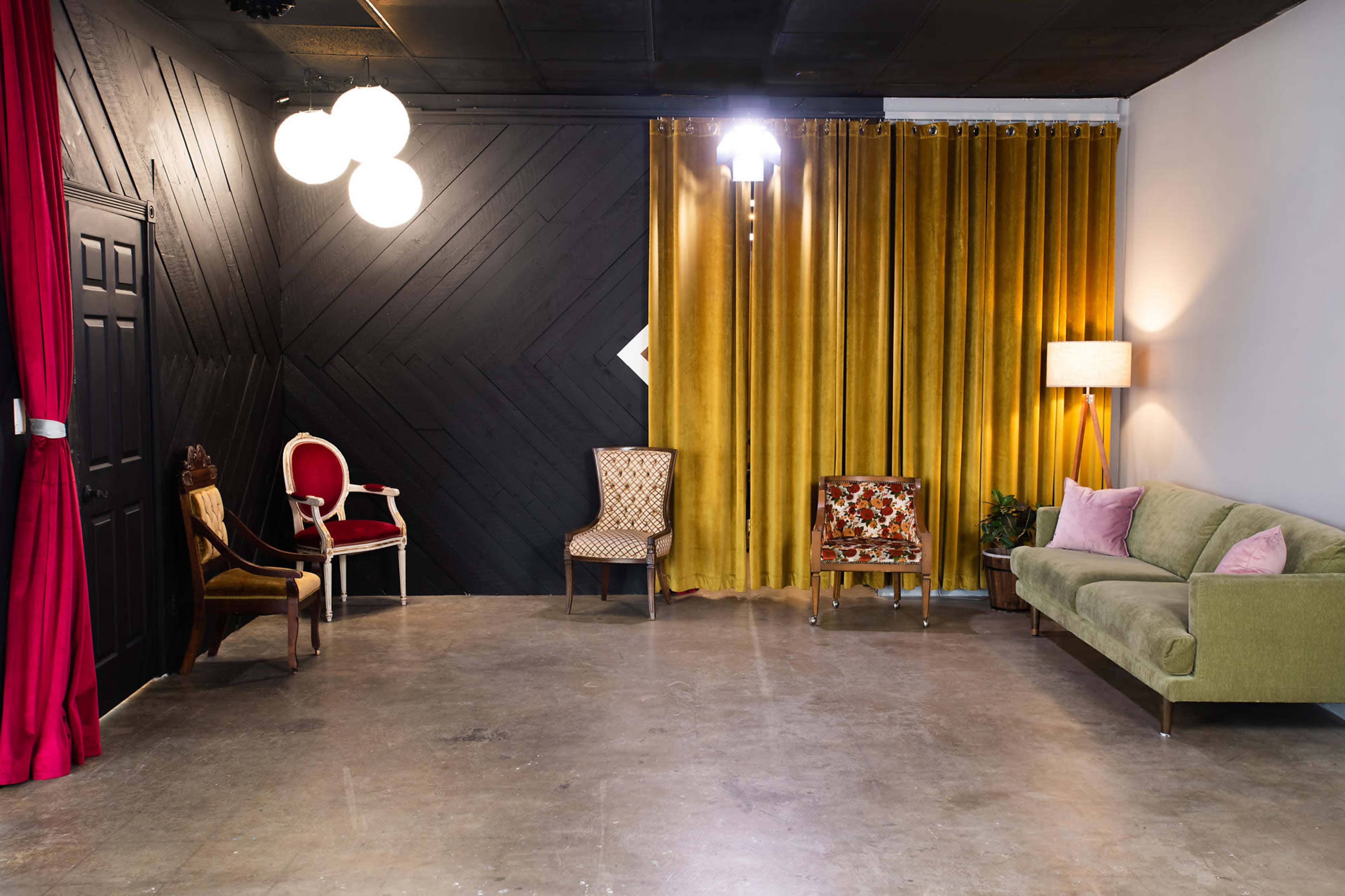 The image shows a modern interior space with a mix of seating options, including a green sofa, patterned chairs, and a red draped curtain, set against a backdrop of dark and light walls.