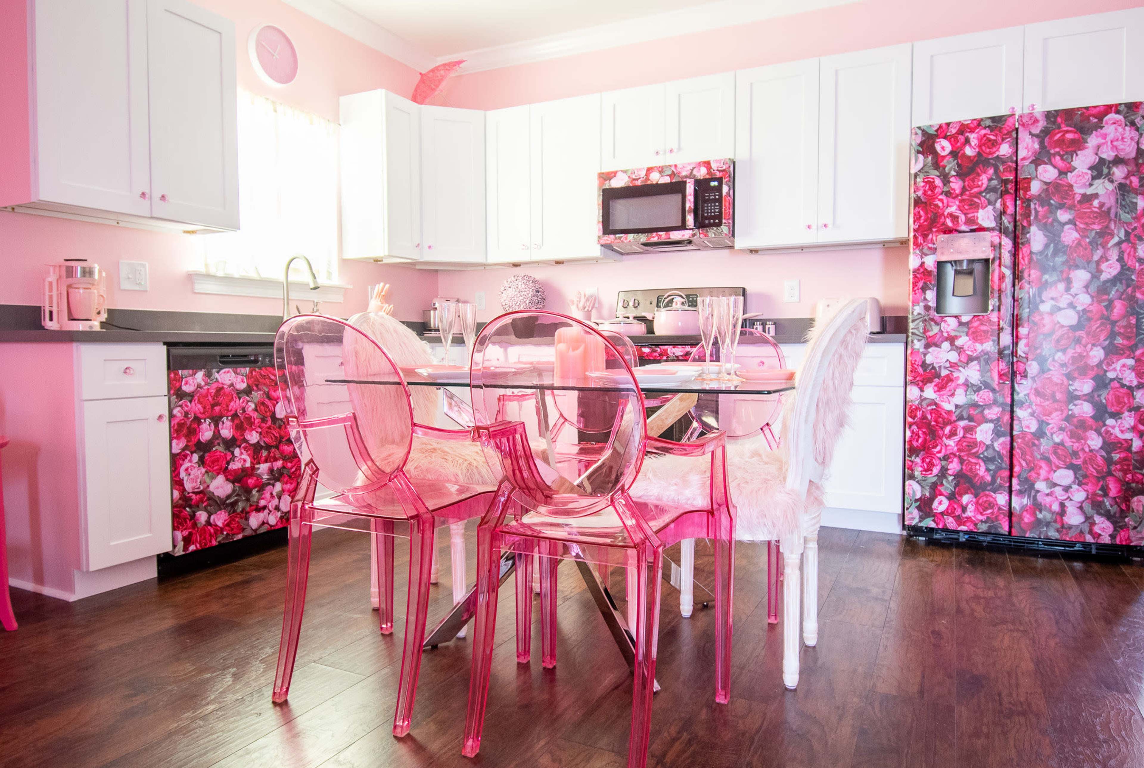 The kitchen features white cabinets and floral-patterned appliances, with a glass dining table surrounded by clear chairs.