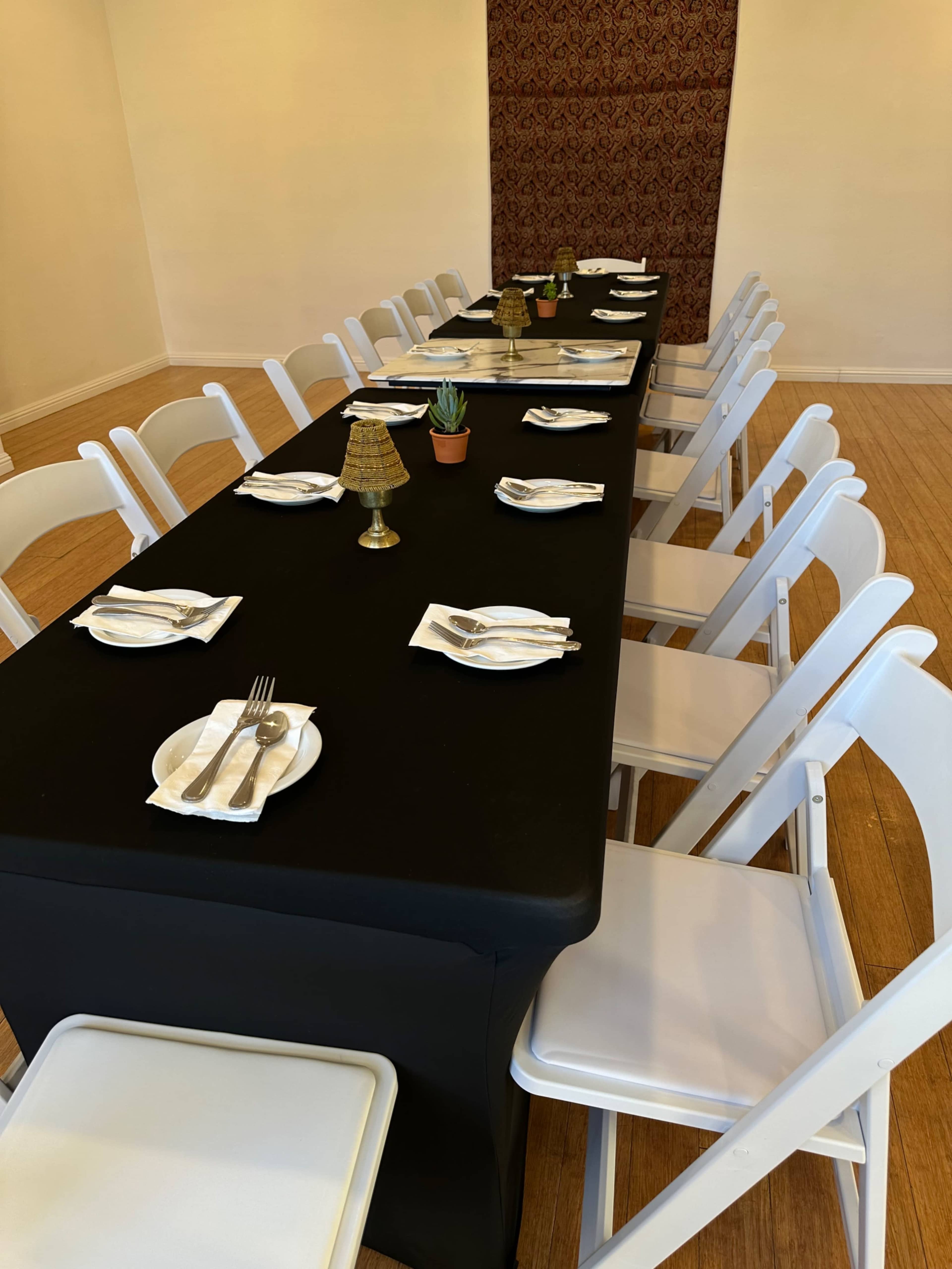 A long black table is set with place settings and white chairs in a well-lit room.