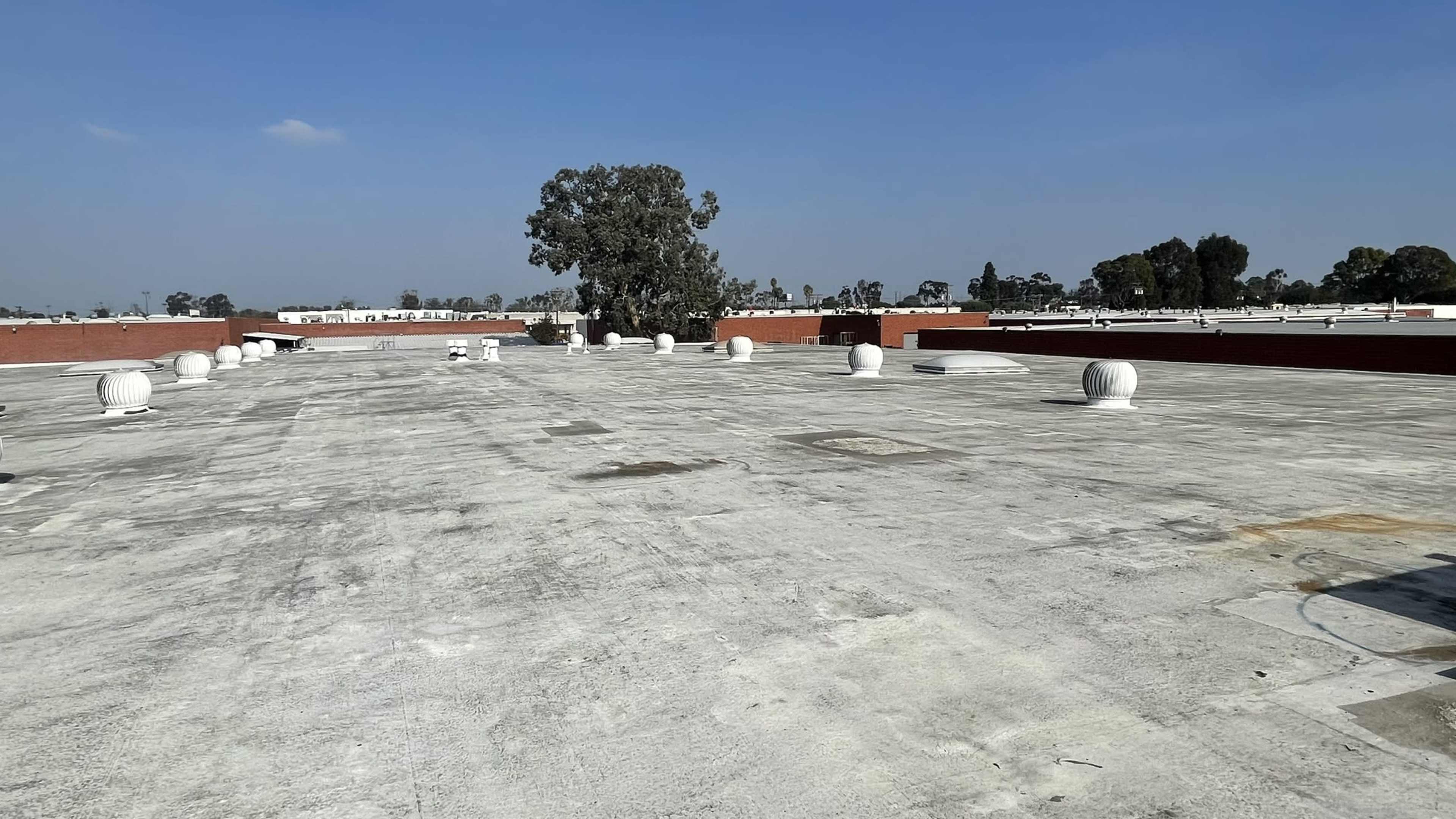 A flat rooftop featuring several ventilation units and a single tree in the background against a clear blue sky.