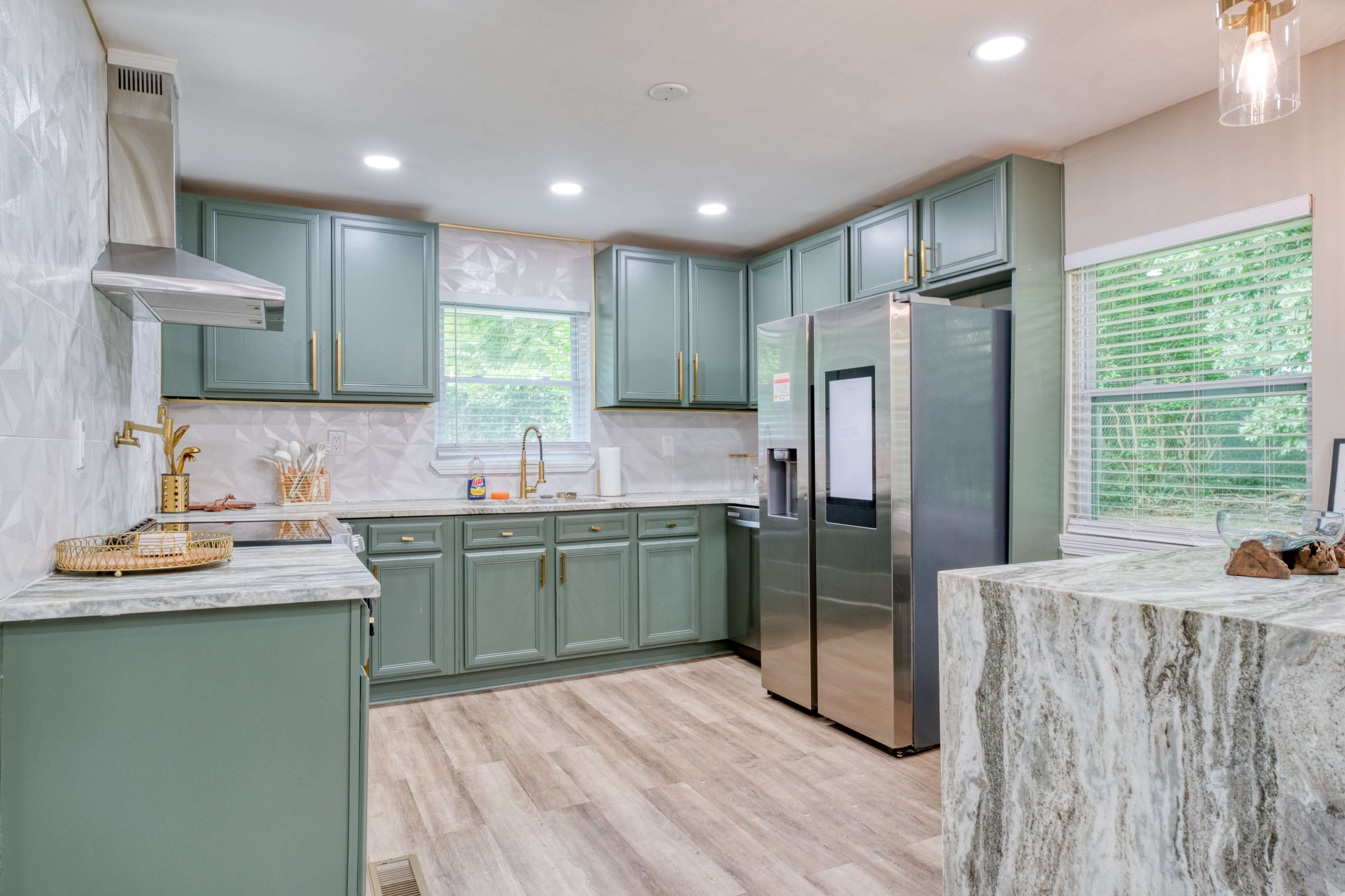 A modern kitchen features green cabinets, a stainless steel refrigerator, and marble countertops.