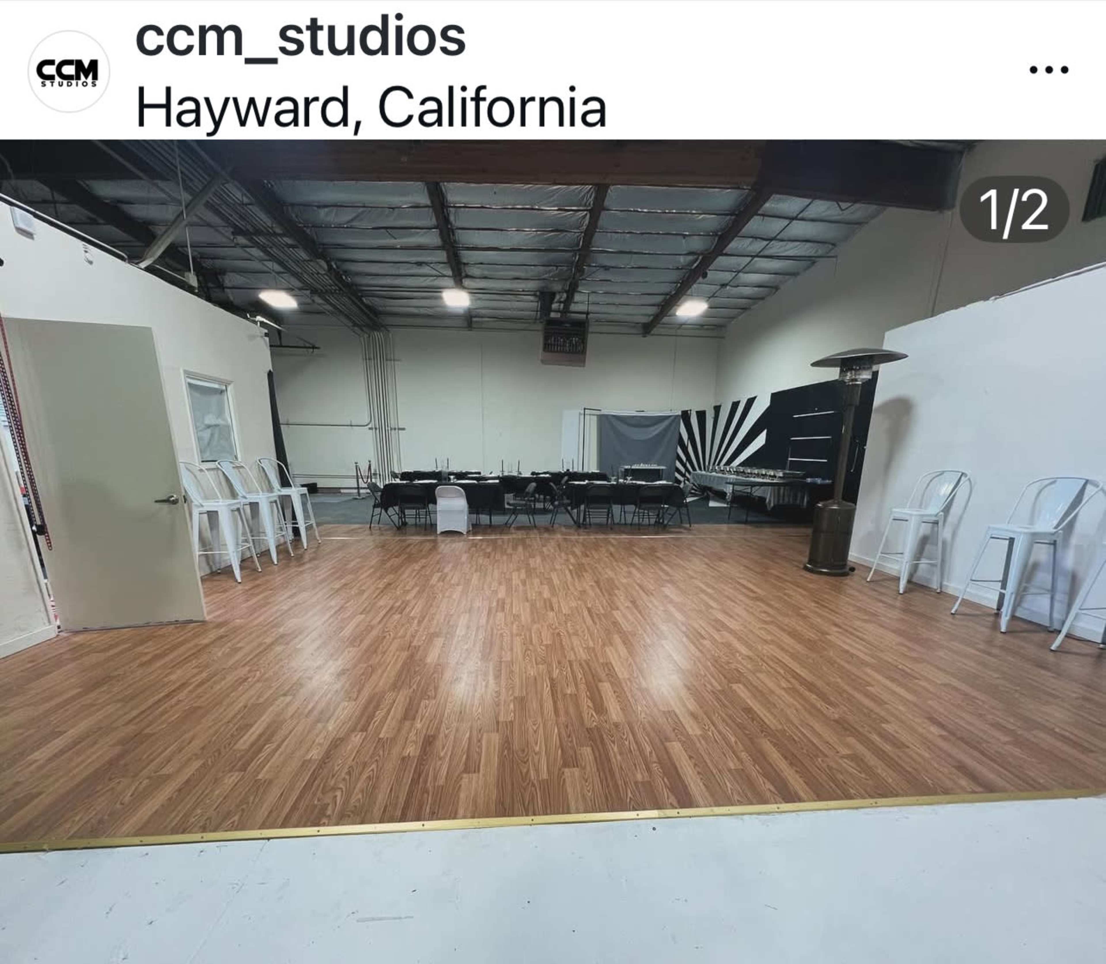 The image shows an empty studio space in Hayward, California, with a polished wooden floor and rows of chairs set up for an event.
