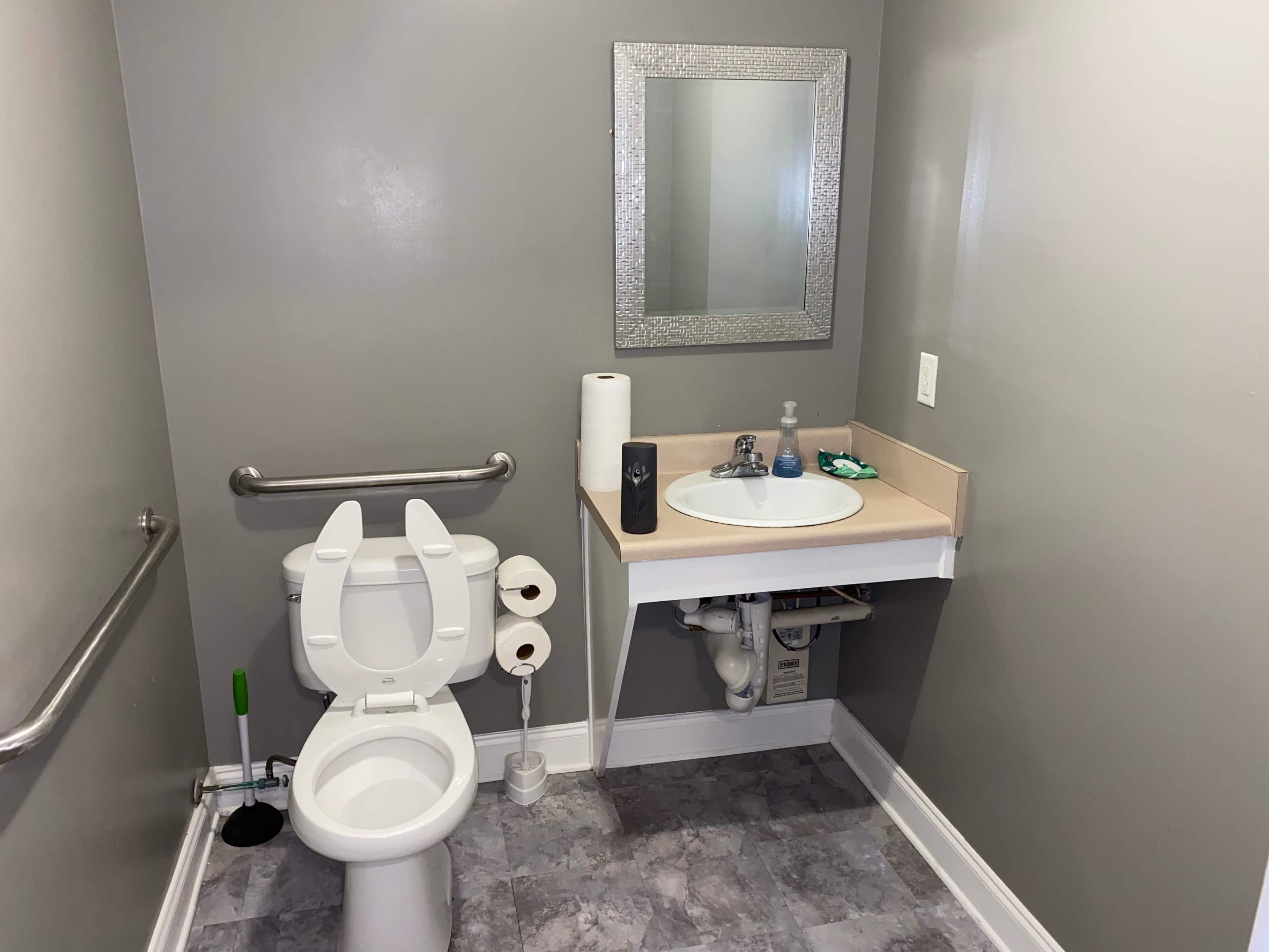 A small bathroom with a toilet, a sink on a counter, a round mirror, and two rolls of toilet paper on a holder.