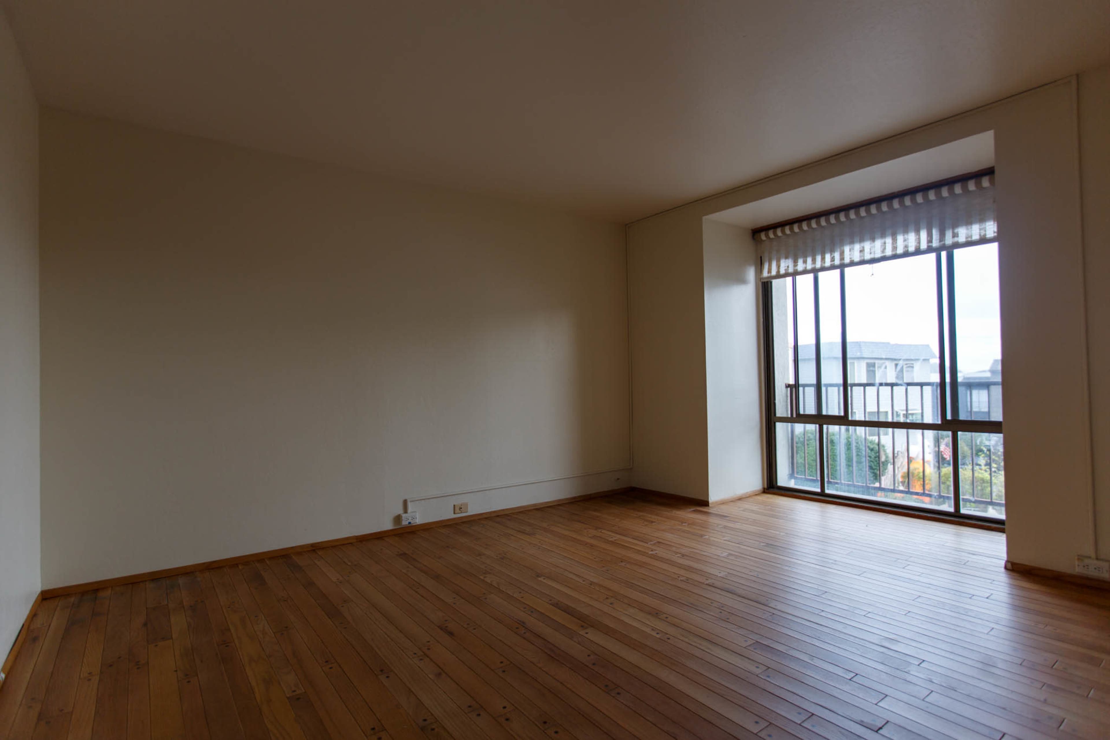 An empty room with wooden flooring and a large window.